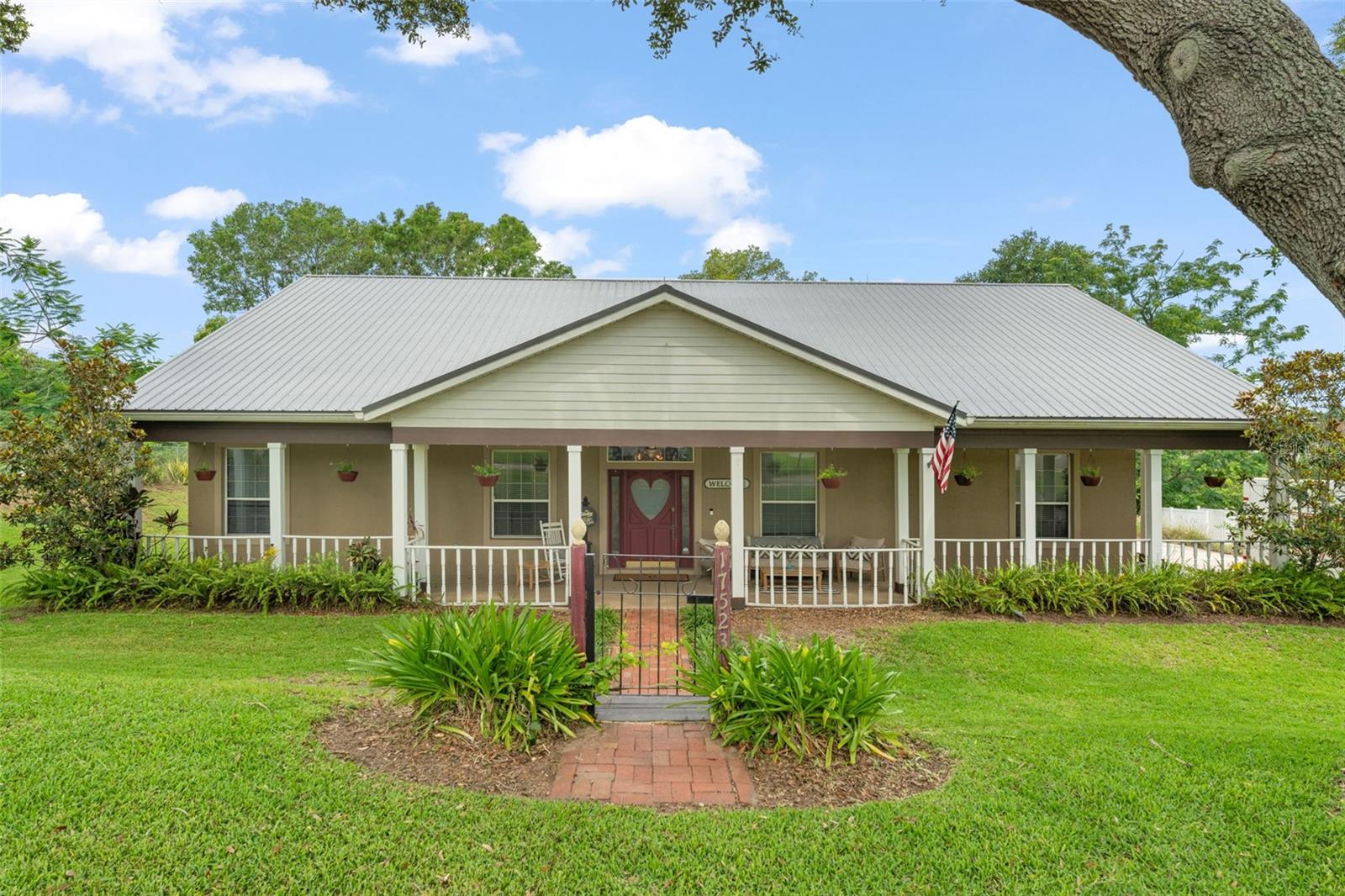 **This property qualifies for a closing cost credit up to $10,300 through the Seller’s preferred lender.** Welcome to a beautifully maintained 5 bedroom, 3 bathroom single-family home in the peaceful town of Montverde, sitting on almost half an acre. This unique property blends rustic charm with modern comfort, offering indoor and outdoor living at its finest—plus a touch of history and artistic flair. You'll be drawn in by mature trees, an expansive front yard, and picture-perfect curb appeal. The home features a wall-to-wall fenced front porch, ideal for relaxing on rocking chairs while enjoying the tranquil surroundings. The standout custom front door, featuring a heart-shaped glass window, is 1 of only 2 original doors from the Minnie Mouse House at Walt Disney World—a truly special piece of Disney history. Discover custom tile mosaics at the front entrance, back door, and in the primary bathroom, adding artistic and personal touches to the home’s character. To the right, you'll find a detached 2-car carport with an adjoining workshop—perfect for hobbies, projects, or extra storage. Inside, a welcoming foyer opens to a vaulted-ceiling living room, where natural light pours in through French doors and large windows. The home includes built-in 7:1 surround sound speakers, perfect for movie nights or background ambiance. To the left is an ideal guest room or office that includes built-in shelving, a closet, and porch views. The split-bedroom layout enhances privacy. On one side, three well-sized bedrooms with built-in closets share a full bathroom with a bathtub and cabinetry matching the kitchen’s warm wood tones. The kitchen features rich wood cabinetry, a carved wood arch above the stove, black and stainless appliances, and a breakfast bar. Just off the kitchen, a cozy dining area glows under a modern chandelier. Behind the kitchen is the spacious primary suite with tray ceiling, private backyard access, and a walk-in closet. The ensuite bathroom includes stone countertops, dual vanities with makeup space, a soaking tub, glass-enclosed tiled shower, and another custom tile mosaic. A third full bathroom with tiled stand-in shower offers access to the back door with direct pool access—perfect for guests. Off this bathroom is a spacious laundry room with a storage closet and ample room for a freezer and fridge. Step outside to your backyard oasis: a screened-in pool, covered patio with wood-burning fireplace, and built-in outdoor kitchen with grill, sink, and bar seating. All just one block from Kirk Park, where Montverde hosts music festivals and Market Days—walkable and even audible from your own backyard. Montverde is a golf cart community, and lucky enough the golf cart conveys with this home—perfect for getting around town, visiting neighbors, or heading to the local park or events in style and convenience. This one-of-a-kind home blends function, style, and storybook charm—don’t miss it!
