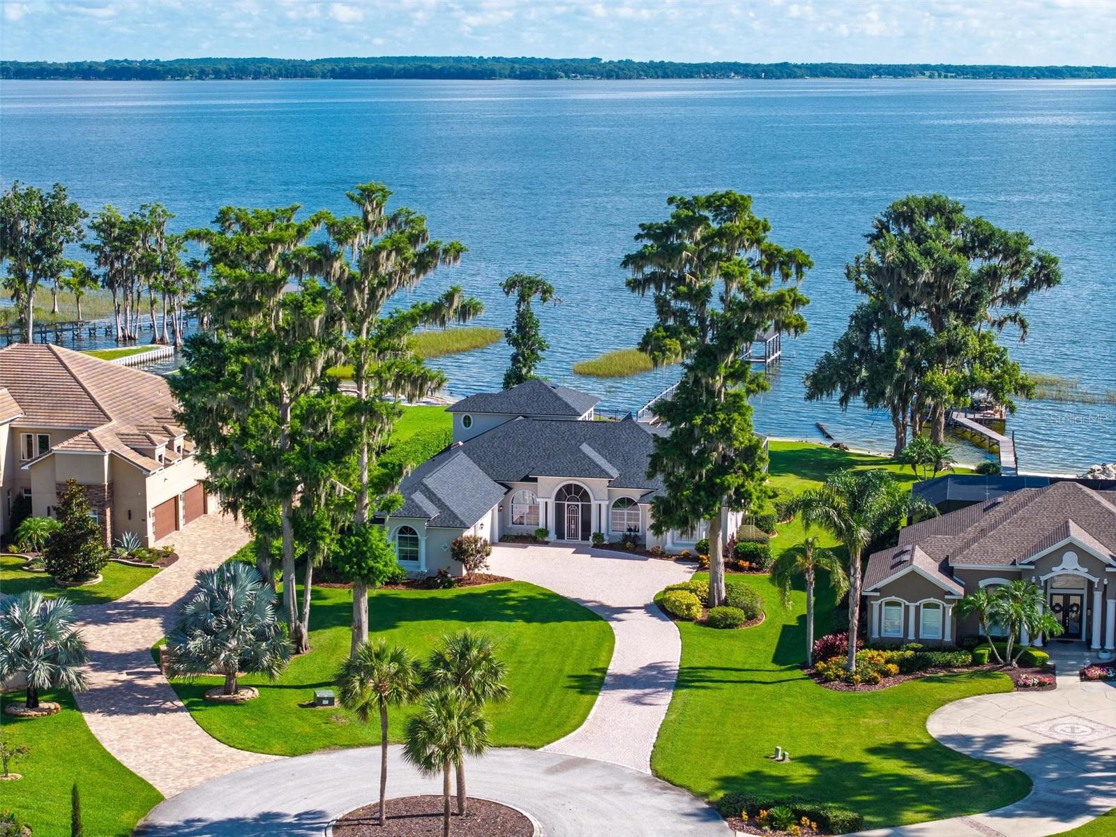 NEW PRICE. Luxury Lakefront Estate on Lake Harris. Offered to the discerning buyer seeking the ultimate in waterfront living. Experience the pinnacle of luxury lakefront living with this extraordinary custom estate nestled on 0.8 acres with 105 feet of pristine shoreline directly on the shimmering waters of Lake Harris—the largest of the renowned Harris Chain of Lakes. Located in the desirable Lakes & Springs community, this private executive retreat offers 4,288 square feet of elegant living space, featuring four oversized en-suite bedrooms (three on the main level), a private home office, and captivating panoramic views stretching over five miles of open water. The estate combines timeless craftsmanship and refined updates, including a brand-new roof and two new water heaters installed in 2024, as well as fresh interior and exterior paint. Inside, the residence boasts a gracious owner’s suite with sweeping lake views, dual walk-in closets, and a spa-style bathroom complete with a walk-in shower and dual vanities. The formal living room with a gas fireplace offers sophistication and warmth, while the chef’s kitchen is appointed with high-end appliances, custom cabinetry, and expansive sightlines over the lake. Multiple living areas include a second family room with mitered glass sliding doors that open seamlessly to the pool and outdoor entertaining area. Upstairs, a fully equipped entertainment suite with a wet bar and kitchenette opens via French doors to a stunning 30-foot covered balcony offering unrivaled lake vistas. The outdoor living experience is equally exceptional, centered around a dramatic infinity-edge saltwater pool with a whirlpool spa, fully Wi-Fi controlled via smartphone. The expansive screened enclosure includes multiple seating and dining zones perfect for entertaining, all while savoring unobstructed views of the lake and direct access to your private boat dock. With daily sunrises and sunsets, along with rich birdlife and natural surroundings, the setting offers tranquility and spectacle in equal measure. Situated on a quiet cul-de-sac just minutes from the iconic Yalaha German Bakery & Beer Garden, and 10 minutes from Mission Inn Resort’s world-class golf, spa, and dining, the home is also a short drive to Lakeridge Winery, The Villages, and charming Mount Dora. Downtown Orlando is just 45 minutes away, with convenient access to both Orlando International (MCO) and Sanford (SFB) airports within an hour’s drive. This home is a rare offering—one that blends privacy, elegance, and recreation in an idyllic lakefront setting. Whether you are seeking a peaceful escape, a luxurious seasonal retreat, or your forever home, 7303 Birds Nest Court delivers an unmatched lifestyle for the most discerning buyer.