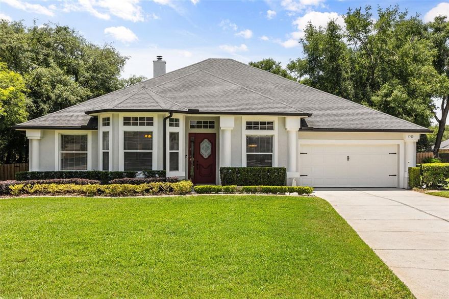 Welcome to 1380 Branch Hill Court, a meticulously maintained home in the gated Sweetwater West community that commands attention from the curb. Set back behind a lush emerald lawn and framed by towering oaks, the soft greige stucco facade is trimmed in crisp white, with stately columns flanking a covered entry and a rich burgundy front door inset with leaded decorative glass. Neatly clipped boxwood hedges trace the foundation, and a wide concrete drive sweeps to the two-car garage.
Step inside to soaring cathedral ceilings, abundant natural light, and warm wood-look tile flowing throughout the main living areas and primary suite. A formal dining room makes an immediate statement with rich navy walls, a recessed tray ceiling, and a dazzling crystal chandelier. A flexible front room serves perfectly as an office, sitting room, or media space. The heart of the home is an expansive open-concept great room anchored by a white-brick wood-burning fireplace and crowned by dramatic vaulted ceilings, purpose-built for entertaining. It flows seamlessly into a chef's kitchen dressed in crisp white shaker cabinetry wrapped in white quartz countertops, a classic white subway tile backsplash, gleaming stainless steel appliances, designer pendant lighting, and an oversized center island with bar seating. The adjacent breakfast nook is framed by tall windows and custom window treatments. The primary suite is a true retreat: rich wood-look tile, sliding glass doors to the screened lanai, and an elegant set of French doors opening to a spa-inspired bath. Inside, indulge in a sprawling double vanity with abundant counter space, a freestanding oversized soaking tub, and a frameless glass shower clad in floor-to-ceiling marble-look tile. A deep, generously sized walk-in closet completes the suite. The secondary bedrooms offer comfortable layouts and ceiling fans, with custom closet organizing systems in two of the three bedrooms, plus the primary closet and kitchen pantry. The dedicated laundry room pairs an LG washer and dryer with a brand-new deep utility sink and vanity. Year-round comfort is dialed in with a smart Ecobee thermostat. Out back, unwind on the screened, covered lanai with ceiling fan and recessed lighting overlooking a massive, fully fenced backyard wrapped in 8-foot privacy fencing, with mature shade trees, generous open space, and room for gardening, pets, a pool, or future improvements. Updated finishes, flexible living spaces, and elevated indoor-outdoor living, this one checks every box. Schedule your private tour of 1380 Branch Hill Court today.