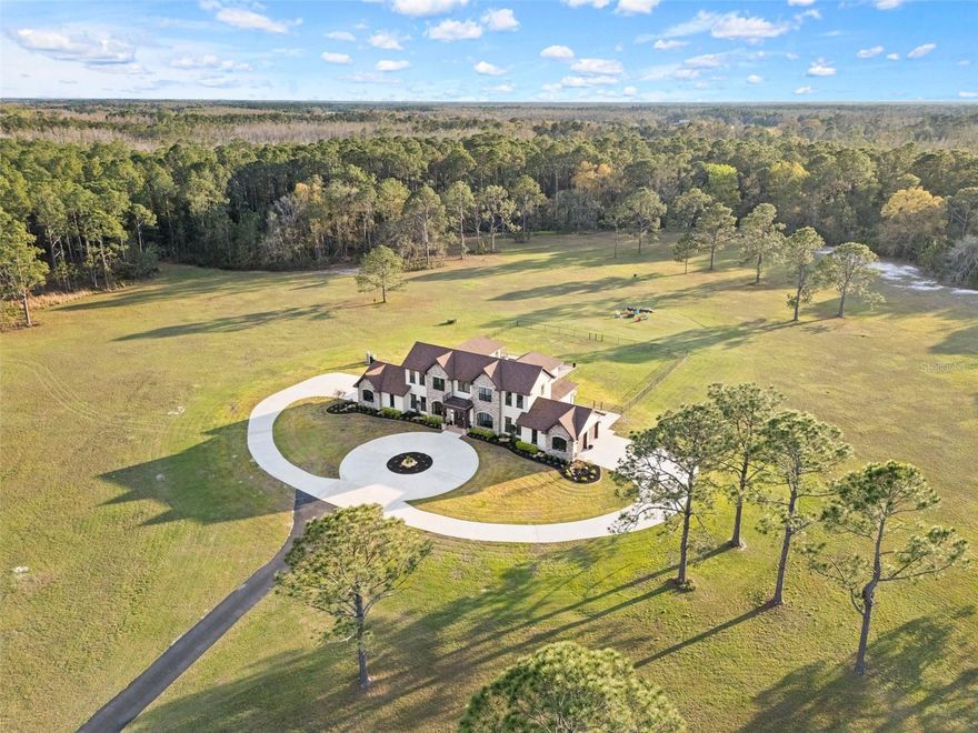 81 acres of glorious seclusion and at the heart your private custom built estate home, elegantly designed and crafted with a versatile floor plan for multi-generational living that includes formal, family, flex and outdoor spaces, your choice of a main floor or second floor primary suite and there is even a hidden pantry for a touch of whimsy! Outside features of the property include: An over 1,000 SqFt zero entry resort style pool with a hot tub and wet pad, 18,000 SqFt asphalt driveway, hurricane windows, dual/split 2-car garages with attic access, whole home Generac system, 1,000 gallon owned and buried propane tank, buried utilities, concrete landscaping borders and a 12-zone watering system for the landscaping. The interior of the home is a light and bright masterpiece of design and functionality delivering; 10’ ceilings throughout / 13’ living room ceiling, 9’ doors, oversized windows with a view in every room, whole home water filtration system, hidden Cat 5 & HDMA cables, custom 3-zone A/C, hickory cabinets throughout, tumbled stone backsplash, soft close cabinetry and drawers, a Maytag commercial washer and dryer with WiFi technology, your choice of owners suites - one on the first floor and one on the second with a wine/coffee bar and fridge to enjoy a beverage on your private composite board balcony, custom shoe closets in both owner’s suites, hidden walk-in kitchen pantry with fridge and custom shelving, engineered hardwood flooring and upgraded spray foam insulation. To say no detail has been missed would be an understatement! With 30+ acres cleared/maintained while the rest remain wild and wooded, this property feels like a personal paradise of native trees and plants right in the middle of Central Florida. You would never know that just minutes away conveniences await - shopping, dining, state parks, lakes and area theme parks and so much more. This level of luxury paired with endless acreage doesn’t come around often - call today to schedule a private tour and be prepared to fall in love with Oak Manor!