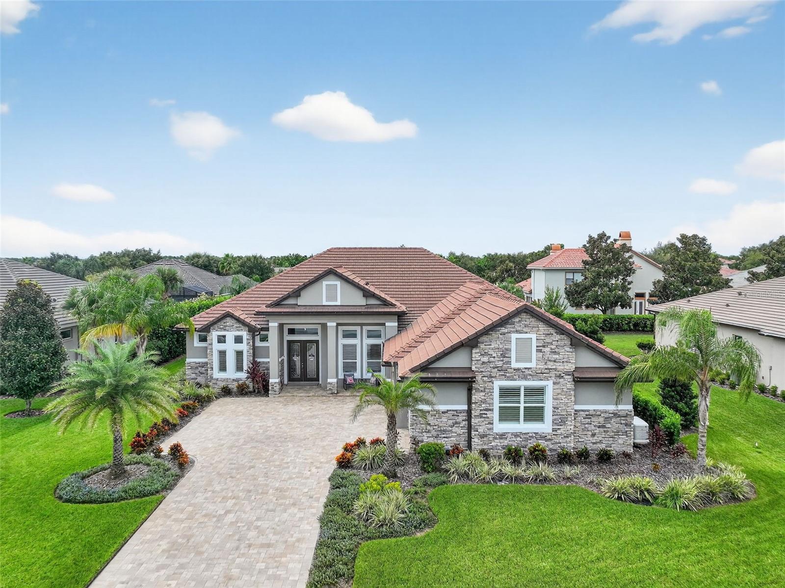 EXCEPTIONAL CUSTOM-BUILT ESTATE HOME IN PRESTIGIOUS LOCH LEVEN OFFERS AMAZING UPGRADES AND A CUSTOM 3-CAR GARAGE. Located 5 minutes from historic downtown Mount Dora is the highly sought-after, gated community of Loch Leven, offering tranquility, beautiful tree-lined streets, and estate homes on spacious parcels. The community setting is rich in natural beauty and borders Lake Loch Leven, a private 169-acre spring-fed lake, which residents enjoy via the community dock and boat launch. Welcome home to your beautifully designed and thoughtfully built home with integrity. At every turn, you'll find attention to detail, high-quality construction, and generous upgrades. The 0.34-acre yard is a carpet of lush grass, featuring palm trees and native Florida plants. The spacious paver driveway and 3-car courtyard-entry garage provide abundant parking for family and guests. Solidly built with block construction and beautifully finished with a stucco and stacked stone facade, a concrete tile roof, and a convenient covered front entry. Leaded glass doors open into a welcoming, bright interior offering a sleek design balanced with warm elegance. High tray ceilings, crown molding, recessed LED lighting, Plantation shutters, and LVT flooring flow throughout. Paint colors, flooring, and cabinet/counter materials are consistent throughout, creating a sense of continuity. All lighting is LED, and upgraded ceiling fans are throughout. Enjoy the energy-efficient benefits of spray foam insulation, including the garage and lanai. West side and exposed South side windows are tinted. Rheem high-efficiency air handler, tankless gas water heater, a 500-gallon propane tank, and a whole-house generator. This home is a dream! The open concept living, dining, and kitchen areas provide a seamless flow for entertaining. The living room tray ceiling adds an extra layer of elegance, and the kitchen boasts high-end finishes. Custom cabinetry, convenient storage drawers, upgraded stainless steel appliances (including a gas 5-burner cooktop), and Quartz countertops are finished off with a stunning Carrara marble backsplash. Upper/lower cabinet lighting, a hidden walk-in pantry, even knife and spice pull-out drawers! The adjacent dining area enjoys lanai views. Open the triple slider door to enjoy the covered screened lanai for parties or relaxation. A split-bedroom floor plan gives privacy for all. The luxurious primary suite features a triple-tray ceiling, lanai access, dual walk-in closets, and a spa-worthy en-suite with dual sink vanities, a free-standing deep soaking tub, and a doorless tiled shower. Bedroom 2 is private with access to a full bathroom and the lanai. Bedrooms 3 and 4 share a full bathroom, and bedroom 4 has a walk-in closet and a private door to the garage. The laundry room has storage cabinetry and a sink. Relax on the private screened lanai with water and gas lines in place for a future pool, pool heater, and summer kitchen. The garage is every man’s dream with loads of space, Shark Shield polyaspartic coated floors, one bay has a tray ceiling allowing room for a car lift, there’s a 30-amp outlet, a mini-split A/C, recessed lighting, a water spigot, a floor drain, and a private door to bedroom 4. Residents of Loch Leven enjoy amenities such as pickleball, tennis, and basketball courts. Convenient to shopping and dining. Easy Orlando commute. This home offers luxury living with everyday convenience.