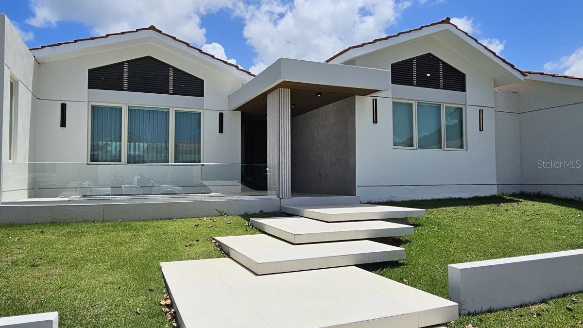 Located in Sabanera Dorado, Puerto Rico, this corner lot with 1,150 square meters of land has a newly constructed and renovated residence that was expanded to 5,800 sf features 5 in suite bedrooms, 5 full bathrooms, and a powder room.
The property features high ceilings and thoughtfully designed living spaces, including a great room, family room, dining area, and outdoor terrace with exquisite tilework throughout. California Closets in all rooms. The design allows for creating an in-law's suite in front of the pool with its own parking and entrance.
The property offers a serene retreat with a sparkling saltwater pool surrounded by lush landscaping. 5 parking spaces plus a golf cart space. Equipped with a 30KW generator, solar water heater, 2,000-gallon cistern and a solar water heater. The kitchen is equipped with Monogram appliances and there are 10 split system air conditioners to climatize all areas of the home. Located within a gated golf cart community, residents enjoy resort-style amenities, including community pools, a gym, tennis and basketball courts, as well as a convenience store, the renowned TASIS school, and 24/7 security