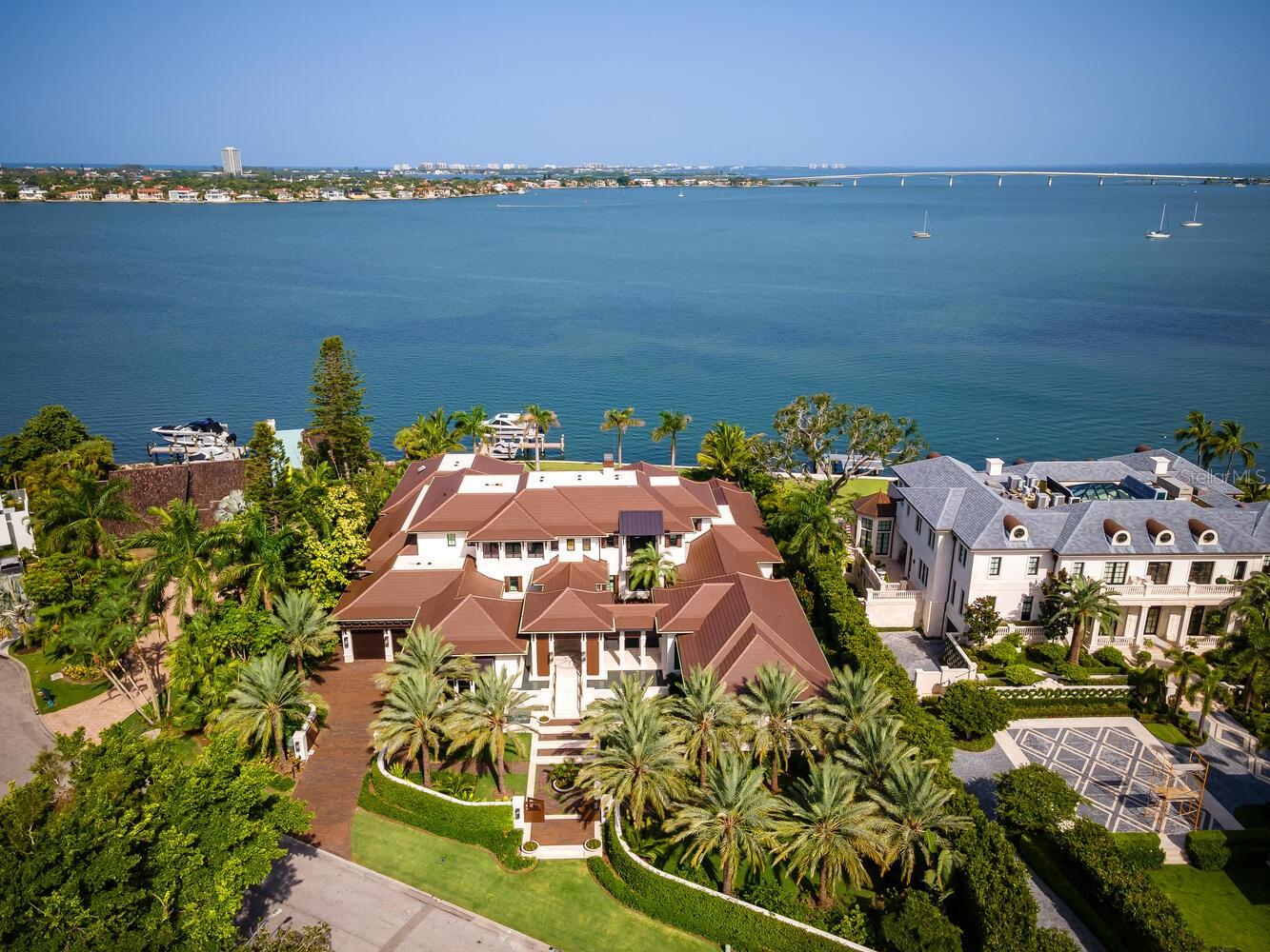 Exceptional in every aspect, this magnificent custom bayfront estate in Sarasota’s coveted Harbor Acres Estate Section showcases superb craftsmanship, state-of-the-art technology, breathtaking vistas and fabulous amenities. Situated on nearly one acre with 144 feet of bay frontage, the 11,275-square-foot home boasts sophisticated, comfortable living spaces, primarily on the main floor, and mesmerizing views of Sarasota Bay, the Ringling Bridge and downtown. The modern British West Indies-style residence has 8 en-suite bedrooms and 4 powder bathrooms. Completed in 2022, the home was designed by Stofft Cooney Architects and masterfully built in 2½ years by Perrone Construction. The meticulously curated estate is perfect for casual gatherings or large-scale soirees. European White Oak Engineered hardwood flooring flows throughout both levels, where architectural ceilings and enchanting light fixtures abound and multiple terraces offer awe-inspiring views. Wolf Design Group of Atlanta masterfully designed the interior. The kitchen, bar and primary bathroom design by Matthew Quinn of Atlanta-based Design Galleria. The remarkably landscaped grounds were designed by Stephen Hazeltine. The stucco and stone accent home features a raised pile foundation, hurricane impact windows and doors, screened covered porch with motorized bug screens and hurricane shutters, and a whole-house generator. Elba White stone steps ascend to an impressive entry pavilion. Inside, refined living spaces await for the entire family, including a voluminous formal living/dining room with fireplace, quartzite feature wall and floor-to-ceiling windows with captivating water views. The 8,200-SF-plus main level also has a dazzling gourmet kitchen, family room, mudroom, playroom, clubroom, gym, primary suite and expansive guest wing. The kitchen showcases an elegant La Cornue range and hood, Sub-Zero appliances and quartzite countertops, with an adjacent scullery, stylish breakfast nook and family room. An enormous temperature-controlled wine display separates the kitchen and formal dining room. The sizable clubroom is ideal for movie and game nights, with a bar and entertainment areas, plus French doors to a bayfront terrace. Elba White stone tile adorns the extensive outdoor space, which offers a kitchen with a Kalamazoo grill, dining and gathering areas, and an overflow pool with spa, sun shelf and fire bowls with automated lighting. A 27,000-lb. high-speed boat lift and 4,500-lb. dual Jet Ski lift with aluminum-framed platform are convenient for launching your waterway adventures. The primary suite features an opulent bathroom with blue quartzite countertops and flooring, massive closet and dressing room, second walk-in closet, morning bar, study and bayfront terrace. The generous guest wing has three en-suite bedrooms, lounge area, patio and a private outdoor entrance. The nearly 3,100-SF second level has a second primary suite, and three guest suites. A large lounge area with a balcony is perfect for savoring the stunning panoramas. Other notable highlights include a Crestron home automation system, motorized drapery/shades, home theater speaker system in the family room and clubroom, Lutron lighting system, whole house generator and automated mosquito spraying system. This waterfront masterpiece is just south of downtown’s dining, shopping and cultural arts, walkable to Southside Village’s restaurants and shops, and a short drive to pristine beaches.