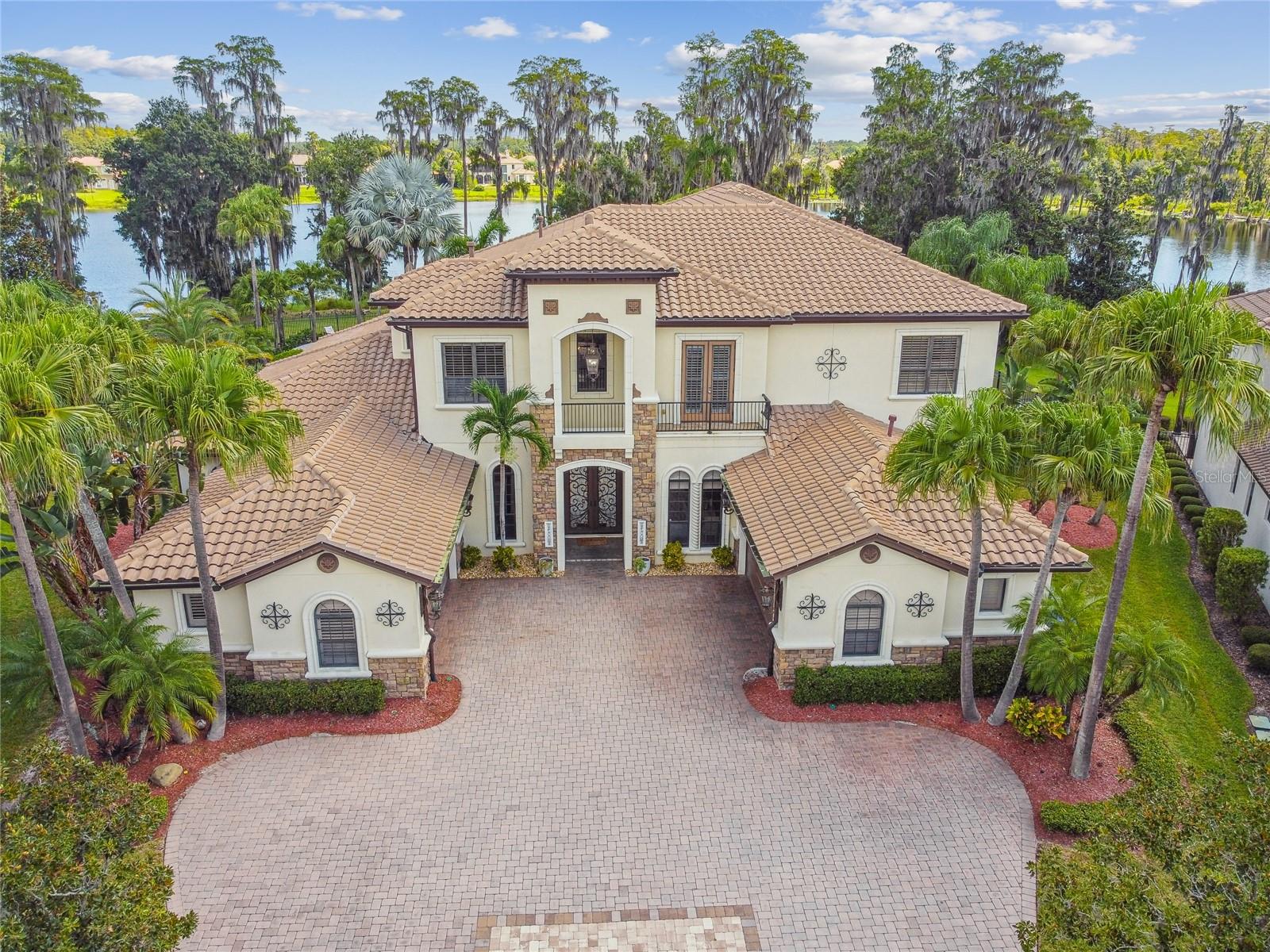 Nestled on a serene lakefront property, this remarkable residence offers sweeping views and unparalleled craftsmanship at every turn. Step into the grandeur of a two-story living space, the heart of intimate family gatherings. Designer lighting, elegant built-ins, a striking stone fireplace, detailed crown moldings, and a splendid wrought iron staircase create an atmosphere of luxurious opulence. The kitchen, a culinary masterpiece, caters to the expertise of two chefs, featuring a 4-burner Wolf range with an integrated grill and a 6-burner Wolf range with double ovens and a convenient pot filler. Custom wood cabinetry, a generously sized pantry, and top-of-the-line Sub-Zero, Wolf, and Fisher & Paykel appliances grace this space, promising culinary delights beyond compare. Entertainment finds its ultimate expression in this residence, with an expansive game room and an adjoining plush theater room designed for eight or more guests. The master suite, a sanctuary of peace, boasts a romantic gas fireplace nestled amidst a cozy sitting area and an indulgent marble bath. Infusing the home with natural radiance are 10-foot glass doors that frame the picturesque views of the lake, lush tropical landscaping, and the outdoor oasis designed for resort-style entertainment. The outdoor area is a vision of leisure and luxury, featuring a captivating pool and spa with a graceful rock waterfall, a sunbathing shelf, and a swim-up dining table capturing the essence of the Florida lifestyle. Adjacent to the pool is a summer kitchen, an inviting outdoor fireplace, and a poolside bath equipped with a sauna and steam shower, creating an ambiance of unparalleled relaxation and indulgence.