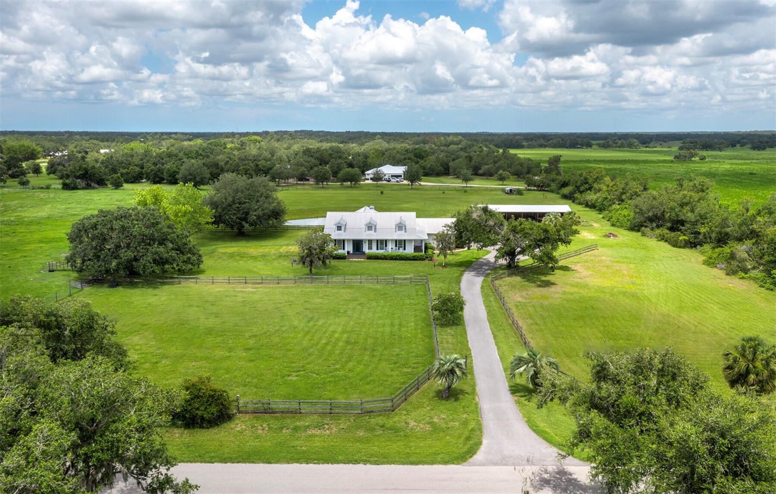 Have you been daydreaming of getting away from the hustle & bustle? Of a home with land, where you can look out your kitchen window and see your horses, cows, chickens, and garden? Well, look no further, because this is absolutely IT. A rare 10-acre parcel with a lovely, move-in ready home, plus a new pole barn with two stalls, all just minutes from the amenities of Sarasota; this kind of property is VERY few and far between. First, let’s talk about the land: a beautiful rectangular parcel where just about every inch is usable, flat, and cleared, the possibilities are endless. Enjoy the two fenced paddocks with their lush grass, 2-stall barn, enclosed garden area, and bass & bluegill-stocked pond just as it is, or add more – maybe some beehives are your pleasure, or perhaps a greenhouse? Other areas are partially fenced so more paddocks will be easy to add if needed and there is space for all of it here! The house is a gorgeous & welcoming Cape-Cod-style farmhouse with a huge front porch. (This is the stuff dreams are made of, seriously.) Soaring ceilings, a rustic stone fireplace, wood flooring, and open & updated kitchen give an elegant feel that also stays nice & cozy. The split bedrooms & extra half bath are convenient, and the size of the main suite will thrill you: a spacious & bright bedroom, 2 big walk-in closets, and an airy, renovated bathroom complete with claw-foot tub – it is just perfect. Sliding doors lead to the huge covered back porch, with plenty of space to lounge, dine, and cook in the magnificent outdoor kitchen, featuring a built-in grill, sink, refrigerator, and your very own pizza oven! There is also an enclosed outdoor shower with hot water just off the porch. Functionally, the property offers hardie board siding, a newer AC, recently re-screened patio, and a brand-new septic field. The house is just 3 miles from the north entrance to Myakka State Park, 15 minutes from the freeway, and about 35 minutes will get you to downtown Sarasota. Don’t wait to see this special home. It is truly one-of-a-kind and, if you love animals, growing & cooking your own food, and plenty of space to breathe, it is the perfect place for your next chapter.