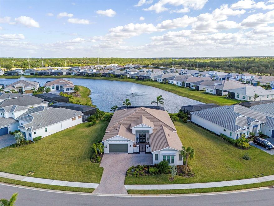 Welcome to a masterpiece of modern elegance, comfort, and sophistication, set within an exclusive and highly sought-after gated community. This luxurious waterside home showcases top-of-the-line finishes and meticulous attention to detail, creating the perfect retreat for both entertaining and everyday living.  From the moment you arrive, the gated front courtyard makes a bold impression, offering both privacy and an inviting sense of grandeur. The property features an expansive four-car garage, ideal for auto enthusiasts or those in need of ample storage space.  Inside, every detail has been thoughtfully designed to elevate your living experience. The home features a massive owner’s suite, a tranquil retreat with custom shelving in its dual walk-in closets for ultimate organization. The gourmet kitchen serves as the heart of the home, boasting an oversized island, numerous cabinetry upgrades, and top-of-the-line appliances, while a reverse osmosis system with a dedicated faucet ensures purified water at your fingertips. Adjacent to the kitchen, you’ll find a functional pocket office, a walk-in pantry with custom shelving, —ideal for entertaining. Throughout the home, custom light fixtures and fans, plantation shutters in the bedrooms and office, and a range of luxury finishes enhance its style and sophistication.  This home is equipped with the latest in modern convenience and security, including a whole-house generator, whole-house surge protection, a robust security system with six cameras, and smart garage door openers integrated with the security system. The electric vehicle chargers in both garages make it future-ready, while the hot water recirculating system and whole-house water filtration and softening system add everyday comfort.  The grand great room is a showpiece of design, with soaring 13-foot ceilings and rich wood flooring, and it flows seamlessly to the outdoors through pocket sliders. The expansive lanai is a true outdoor retreat, featuring a pool and spa illuminated by custom lighting, a convenient cabana bath, and a view of the stunning fountain that lights up at night, creating a serene ambiance against the backdrop of tranquil water views.  With three spacious bedrooms, a large bonus room complete with its own private entry and wet bar, and a thoughtfully designed custom laundry room, this home offers unparalleled versatility and comfort.  This home truly exemplifies luxury waterside living, blending modern convenience with timeless design. Schedule your private tour today and experience the unmatched elegance of this extraordinary home!