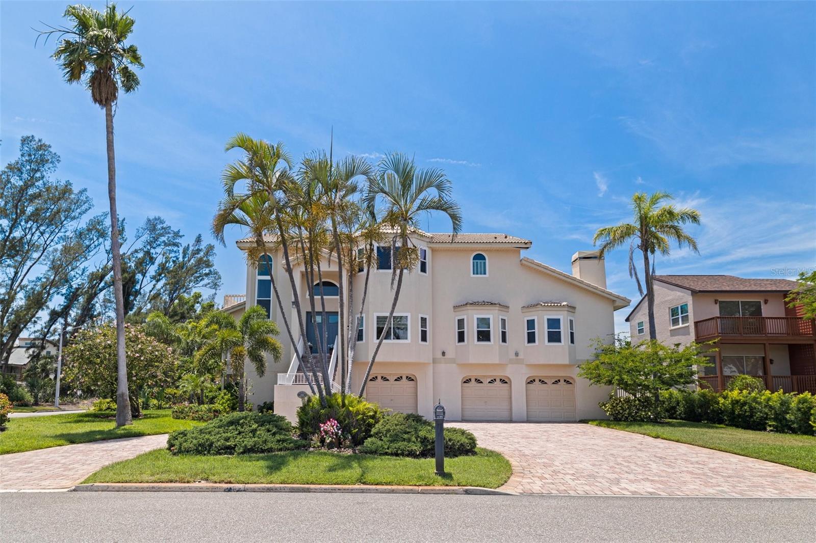 Island Living on an Oversized Corner Lot in this expansive four-bedroom elevated residence offers generous living and entertaining spaces, set on a rare oversized corner lot in a sought-after island community. While not waterfront, the upper levels reveal partial views of Tampa Bay, enjoyed from the new high impact windows and multiple vantage points throughout the home.
As you arrive, the oversized circular paved driveway welcomes you home. Ascend the elegant front staircase to the newly installed high-impact rated front door, a great entry point leads into a contemporary, sunlit, open floor plan featuring high ceilings. Thoughtful interior flow seamlessly connecting your formal dining room, spacious living area, and an elegantly freshly updated kitchen with white cabinetry, quartz countertops, pull-out drawers, and new stainless appliances. Large island allows for comfortable breakfast bar seating. The adjoining family room, with its cozy wood-burning fireplace and new window treatments, flows seamlessly to the relaxing outdoor balcony overlooking the lushly landscaped yard and oversize pool.
The main level includes a guest bedroom (or office) with adjacent full bath, while the oversized primary suite boasts balcony access, a generous walk-in closet, and a spa-inspired bath with Jacuzzi tub and large walk-in shower.
Upstairs, you’ll find two additional bedrooms with its own closets, a full bath, and a secondary living area—ideal for lounging, watching tv or use as a game room. Beautiful views or Tampa Bay from the top floor! The ground floor offers over 2300sf of an impressive multi-car garage with workshop, bonus room, and direct access to the pool with spa and shaded patio, creating a perfect space for hobbies or entertaining.
Ideally located just 15 minutes from downtown St. Petersburg and close to award-winning beaches and dining, this beautifully maintained home offers the space, flexibility, and lifestyle of true island living.