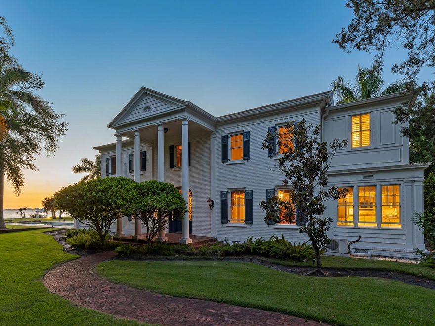 This storied waterfront estate occupies a 1.24-acre lot within the largest contiguous parcel on the Gulf Coast, a magnificent private park with a majestic landscape and vistas on par with Selby Gardens and the grounds of the nearby Ringling Museum. Renowned for its historical significance and stately Southern Colonial architecture, the Earle House presents a rare restoration opportunity to customize modern luxury with the provenance and style of old-world elegance. Encompassing both a two-story primary home and separate garage and guest house, the estate offers spacious accommodations for enjoyment as a seasonal retreat or year-round residence. Priced with consideration for renovations, this property is both comfortably livable and poised for thorough personalization. 
Distinguished by a double-height colonnade and beautiful brick exterior, the 4-bedroom, 4.5-bathroom home boasts original classical features throughout, including wood paneling and crown moulding, hardwood floors, fluted balusters, gas fireplaces, large chandeliers, stained glass transom, double-hung windows, and French doors. Built in 1927 and renovated to modern standards in the 90s with additional projects in following years, the home’s upgrades include a waterfront saltwater pool, elevator, walk-in showers, and top-line appliances.
Flanked by leaded glass window panels, the south-facing main entry opens to a grand foyer that leads on one side to the dining room and on the other to the waterfront great room and adjoining solarium. Awash in natural light from both south- and north-facing windows, the great room is anchored by a large central fireplace with granite hearth and an ornately carved mantle, with access at one end to a private wood-clad den with powder bath. Subtly partitioned from the great room by a coffered beam, the adjacent solarium seamlessly extends the main living space and spectacular vistas with a surround of oversized windows and double doors that open to the pool terrace and waterfront lawn. On the east side of the main floor, the foyer opens to the spacious dining room with two original arched door corner cupboards and a well-appointed wet bar that adds ample storage as well as additional under-counter refrigeration and dedicated beverage cooler. Beyond the dining room, a breakfast nook opens to the roomy kitchen.
Upstairs, a spacious landing leads to three large bedrooms, each with incredible views. To the right, a private alcove with elevator access leads to the western-facing primary suite with a massive brightly lit bedroom, walk-in closet with custom built-in wardrobe system, and a marble-clad bathroom with oversized vanity and walk-in shower. On the other side of the landing, two additional bedrooms offer generous layouts.
The history of the Earle House is integral to Sarasota’s early 20th-century development, dating to the formation of the Indian Beach community with the sale of magnificent waterfront homes to affluent families from across the United States. This remarkable estate, enviably near the Ringling Museum and Asolo Theatre, stands on an indescribable piece of land with more than 130 feet of private waterfront, winding paths, and a palm grove complementing the lush tropical landscape. With adjacent parcels available by separate offer, this is an opportunity to acquire the largest acreage on the Gulf Coast, rich in architectural history and unmatched in natural beauty.