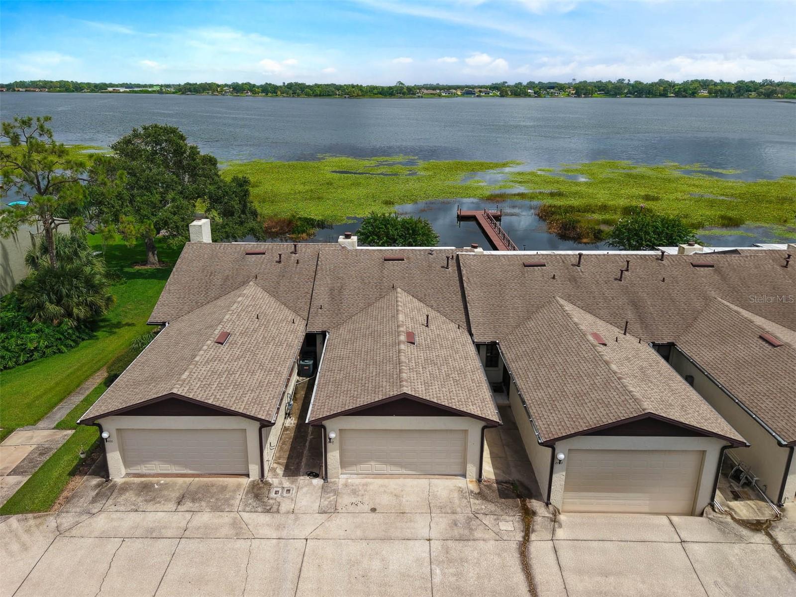 Lakeside living, front-row. This 3-bedroom, 3-bath townhome sits directly on Lake Hartridge—part of the Winter Haven Chain of Lakes—in an intimate, 28-unit community with a dock right out back and postcard views from both levels. Two expansive screened lanais run the width of the home, so morning coffee, afternoon breezes, and sunset watching all happen with the water as your backdrop. Entering on the second floor, where light fills the open living and dining areas anchored by a fireplace, and sliders extend the space on to the lanai, all designed to capture the stunning lake views. The kitchen keeps everything connected and recently added a crisp backsplash and a new refrigerator. Also on this level: a full bedroom, full bath, and a spacious walk-in pantry or utility closet—ideal for guests or multigenerational living. Downstairs, the lake takes center stage. The oversized lower lanai walks out to the lawn and community dock. Two additional bedrooms (one with direct lanai access), two full baths (including a spacious ensuite), an office/flex room (which can be used as an additional bedroom), a laundry room, and excellent closet storage make this level work hard for everyday life. Tile flooring runs throughout most spaces, with new carpet in two bedrooms. Updates that matter: new roof; two new A/C units (one per floor; both installed June 2024); fresh interior paint and new carpet; two new fans on the upstairs lanai; new kitchen backsplash; new shower door (downstairs); new blackout blinds plus wooden blinds in the upstairs bedroom; and new cameras for peace of mind. Community perks keep it easy: HOA covers pest control, grounds maintenance, pool access, trash, recycling, cable, and internet. Lake Hartridge Park and the public boat ramp are close by, giving you instant access to the Chain. Quiet, convenient, and all about the water—this is the lakefront lifestyle, done right.