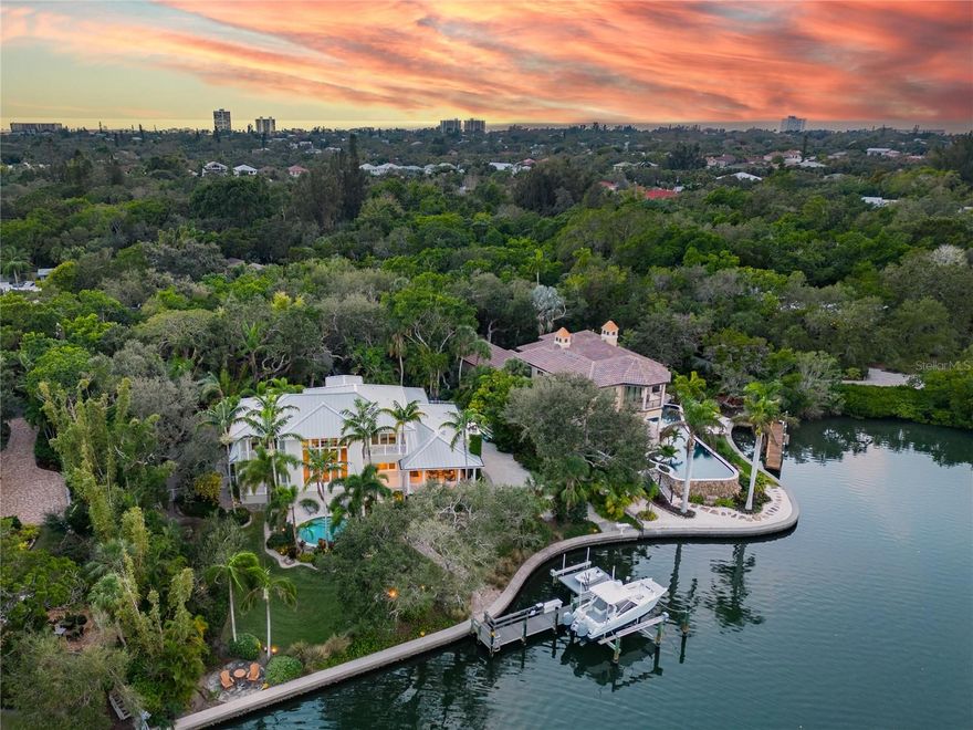 Nestled within Siesta Key’s exclusive neighborhood of Hidden Harbor, a tree canopied intracoastal neighborhood with just 36 residences, awaits a breathtaking private oasis on .72 acres. Step inside and admire the meticulously crafted interior featuring newly refinished wide plank white oak flooring and custom millwork. Soaring ceilings will impress while a wall of windows will draw your attention to the backyard paradise where palm trees shade the sparkling, salt water circular pool. 
The opulent kitchen will inspire your culinary creations while friends and family gather around the oversized island and adjacent dining area. Custom, hickory cabinetry provides ample storage while the Silestone and granite counter tops sparkle under the updated recessed lighting. The top-of-the-line Sub-Zero refrigerator and Wolf cooktop/oven will delight the most discriminating chef. 
Retreat to the primary suite with a private outdoor terrace and spa-like bath featuring a walk-in shower, soaking tub and large walk-in closet. Upstairs you’ll find an office/den and 2 en-suite guest bedrooms both with private terraces and beautiful views. 
Invite your guests to enjoy the Suncoast lifestyle where mature trees provide privacy for your elegant, covered patio with shell stone flooring, a gas-assist wood-burning fireplace, graceful cypress ceilings, cozy seating, a fully equipped outdoor kitchen and breathtaking views of the shimmering waters of Robert’s Bay. 
Other noteworthy features include Lutron treatments on all first floor windows; whole-house Sonos surround sound; a comprehensive security system; 27kW generator; 2 AC units with 5 zones; hurricane rated exterior doors and windows; a 153’ seawall (installed in 2011); a 50’ dock; two remote-controlled boat lifts (10,000-lb & 16,000-lb); an oversized 2-car garage; and an irrigation well. 
Situated close to the prestigious Out-Of-Door Academy on the highly sought after Siesta Key, well known for its vibrant island culture and the world famous Crescent Beach, find yourself centrally located to all that is the quintessential Florida lifestyle. Wander to one of the gulf coast barrier islands for a day of lounging by the water, explore the arts and shopping of downtown Sarasota and St Armands Circle, or enthuse in the many recreational opportunities that the area offers from golf to wildlife watching. This exceptional home offers a seamless blend of luxurious indoor living and a captivating outdoor ambience, creating the perfect space for relaxation, entertainment, and creating lasting memories.