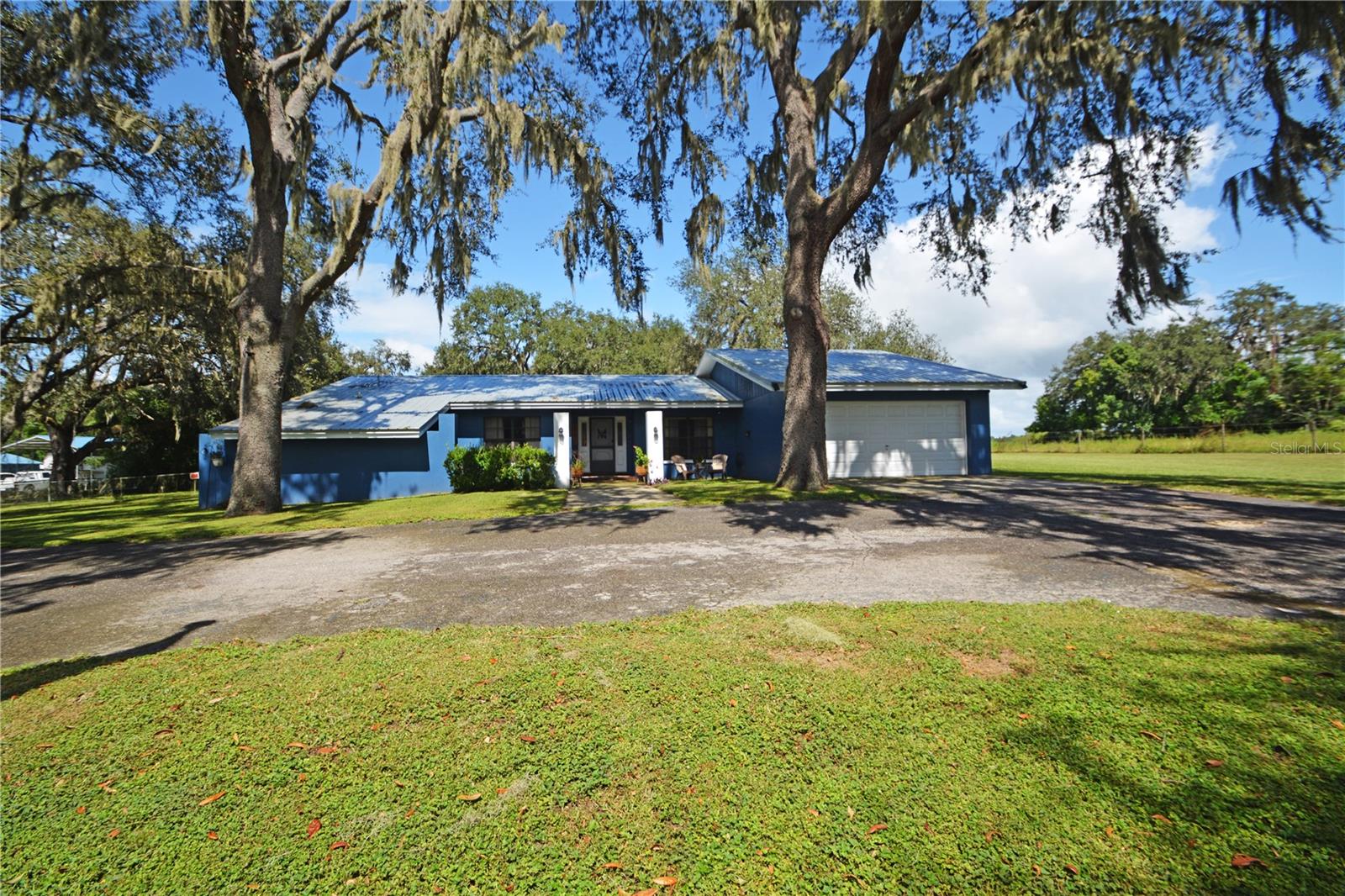 If having space between homes, a screened-in lanai overlooking an extra-large yard with enough space to turn it into your own private oasis, and a hobby workshop or mancave sounds ideal to you, then you'll want to view this home. Located less than a mile from the city limits of the growing yet quaint town of Zephyrhills, on 1.45 acres, this single-family home with a generously sized workshop is ready for new owners. The circular paved driveway lends an aesthetic appeal to the home’s entrance and allows for easy entertaining. The well-kept wood floors span in two directions from the entrance area to the formal living room and dining room. The formal living room has sliders that open up to the screened lanai. The dining room is conveniently located just off the spacious kitchen. There’s plenty of cabinetry, countertop space, and a pass-through window over the sink connecting to the outdoor grilling area. The kitchen and its eat-in area overlook the oversized family room and the wood-burning fireplace. The family room's sliding doors connect it to the lanai, creating a circular flow for entertaining. The interior has a 3-bedroom, 2-bath floor plan. The primary bedroom with two closets, one a walk-in, overlooks the backyard through sliding doors and has direct access to the lanai. The mud room, located at the garage entrance to the home, provides an extra storage area. The separate workshop has a two-car garage door and is 30 ft by 36 ft. There is a 20 ft by 30 ft covered area extending off the side of the workshop, more outdoor activity space, and another 12 ft by 30 ft covered area. It’s waiting for an RV or a garden of plants needing part shade. The home has smart features. They include not only the home but the workshop. Both can open and close garage doors and the front door, making life easier. There is enough space to add a pool, have a fire pit for those chilly fall evenings with s'mores, and still have plenty of room left for two and four-legged ones to run around. Locally owned stores like the Zephyrhills Community Pharmacy, along with the familiar Starbucks, Lowe’s & Ace Hardware, Panera, and many other businesses, are a very short distance away. This home is the perfect spot to relax on the lanai, starting your day with a cup of joe and ending your day with your choice of spirits, or listening to the gentle sounds of the rain hitting the 2017 metal roof overlooking whatever you envision in your new backyard. Don’t miss out on the opportunity to own this property; in 7 to 10 years from now, you may wish that you did.