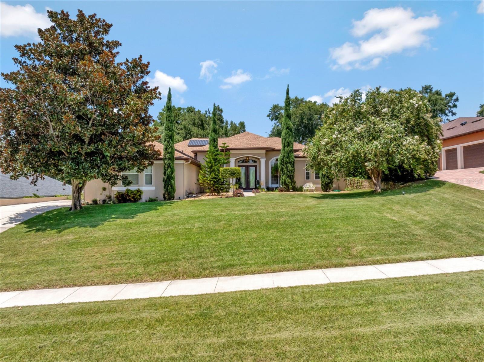 Welcome to this Montverde beauty situated on over half an acre with fully paid-off solar & stunning curb appeal. From the moment you arrive, this home makes a statement. Framed by mature trees and manicured landscaping, this 4-bedroom, 3-bath gem sits proudly on over half an acre, overlooking stunning rolling hills in the highly desirable town of Montverde, just minutes from the renowned Montverde Academy and the exclusive Bella Collina Golf course. With over 2400 sq ft of living space, this home offers a split floor plan that blends function with flow. Natural light pours through the large windows highlighting the soaring ceilings and elegant architectural details. The 2022 roof and fully paid-off solar panels mean big savings and peace of mind, with average electric bills around just $35/month. The oversized 3-car garage gives you all the room you need for vehicles, storage, or even a workshop. Out back, the paver-lined covered porch and built-in firepit create the perfect setting for evening hangouts! With over half an acre there’s still plenty of room to add a pool, expand your garden, or anything else your heart desires. If you’re looking for a small town feel close to big-city conveniences, Montverde is the place for you.
