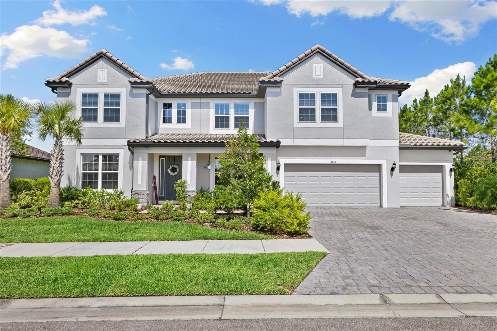 Price reduced due to out-of-state relocation!! Experience refined luxury in this nearly new, highly sought-after Watergrass residence, offering expansive panoramic pond views and stunning sunsets in Wesley Chapel, Florida. Ideally situated on a premium lot adjacent to the exclusive neighborhood park and within the secure gates of the Graybrook subdivision within the Watergrass neighborhood. This home encompasses approximately 5,452 square feet. It features seven bedrooms, four full bathrooms, and two half baths, a 5-car garage including two main-level bedrooms—one suitable as a guest suite—as well as a study, and a Dining room. Two Laundry rooms, one on each floor, each with a deep utility sink. There is a third large utility sink located in the garage. The home is prewired for generator backup and upgraded electrical service. Enjoy over 300 sq ft of patio space, a heated, oversized pool/spa with a large paver deck, teak ceilings, enhanced lighting, three outdoor ceiling fans, and modern indoor-outdoor living. The interior features an expansive great room and a state-of-the-art gourmet kitchen, equipped with quartz countertops on a large double waterfall island, custom cabinetry with pull-out drawers, a pot filler, a stylish tile backsplash, an oversized pantry, and premium appliances, including a gas cooktop. Custom lighting and custom woodwork accentuate the sophisticated atmosphere. The primary suite serves as a private retreat, complete with his and hers walk-in closets, a luxurious ensuite bathroom featuring quartz countertops, an oversized frameless glass shower with three shower heads, and a two-person soaking tub. The upper level includes a spacious rec room with a wet bar, a theater room (Bedroom 6), and a fully equipped home gym (Bedroom 7). Additional amenities include a propane tank, a tankless gas hot water heater, custom paint, in-ceiling surround sound speakers in the theater room with a soundboard wall feature, and more. Advanced smart home appliances and technology include a Ring doorbell, security cameras, Wi-Fi extenders, and programmable outlets for holiday lighting. The neighborhood features a clubhouse with a gym, a large pavilion, multiple pools, a splash pad, and tennis courts, as well as top-rated schools. With shopping, dining, and easy interstate access nearby.