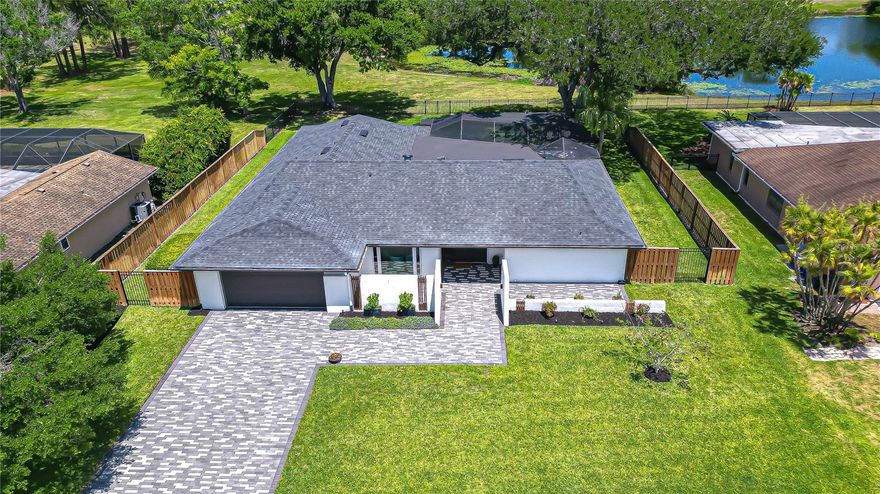 Prepare to be absolutely WOWED from the moment you arrive—this Carrollwood Village showstopper makes an unforgettable first impression. A beautifully designed brick paver driveway with elongated pavers in striking alternating gray tones creates a custom approach, continuing to a paver walkway and two inviting front patios flanking the entrance. A lush, manicured lawn and thoughtfully curated landscaping set a picture-perfect stage, while an impressive solid wood double entry door and side window establishes a grand, welcoming presence. This exceptional 4-bedroom, 3-bath home spans 2,663 sq ft of living space, perfectly situated on a spacious .36-acre homesite with a private pool and lanai, beautifully fenced backyard, serene pond views—your private retreat.
An expansive open floor plan welcomes you with a gracious foyer featuring a coat closet and a custom built-in bench seat. The home unfolds into a light-filled, airy space where a picture window frames the elegant dining room, seamlessly connected to a stylish wet bar with cabinetry, a beverage refrigerator, rich wood countertop, vessel sink, and upper display shelving—perfect for entertaining. The living room captivates with a built-in wall fireplace beneath a dedicated TV niche, while four panel sliding glass doors flood the space with natural light. Luxury vinyl plank flooring flows throughout the main living areas, complemented by fully integrated Smart recessed lighting for a refined, modern feel.
The kitchen is a true showpiece, where thoughtful design meets striking style. A recessed ceiling adds architectural depth, while sleek Shaker cabinetry accented by an elongated subway tile backsplash creates a clean, sophisticated aesthetic. Exotic Sandstone countertops extend to a breakfast bar, blending form and function, alongside a suite of high-end Samsung appliances. A deep farmhouse porcelain sink, perfectly positioned beneath a window, overlooks the lanai and pool, bringing in natural light and tranquil views. Just beyond, a beautifully appointed laundry area evokes a butler’s pantry, featuring galley-style cabinetry, matching sandstone surfaces, a coordinating backsplash, and additional storage.
The family room offers an inviting yet dramatic space, highlighted by a soaring vaulted ceiling and a custom built-in entertainment wall with lower and tall side cabinets. Another set of four panel sliding glass doors enhance the natural light and create a seamless connection to the outdoor living area. Privately situated, the spacious primary suite features a sitting area and direct lanai access. A custom dressing hallway lined with built-in cabinetry leads to the luxurious ensuite bath, complete with dual quartz vanities, a pocket door for added privacy, and a beautifully tiled glass-enclosed shower with a frosted window for natural light.
Secondary bedrooms are thoughtfully arranged within the 3-way split layout, accompanied by two modern baths, including a convenient pool bath, while a hallway coffee bar adds a touch of everyday luxury. Outdoors, the lanai is a true retreat, showcasing a plank ceiling, marble pool deck, and a striking geometric-style pool with sun shelf and bubblers, all within a newer screened enclosure. The lush, green backyard is fully fenced with gated entry and an aluminum fence along the rear, perfectly framing peaceful pond views and creating a private, resort-style escape. Experience this exceptional home in person—schedule your private showing today.