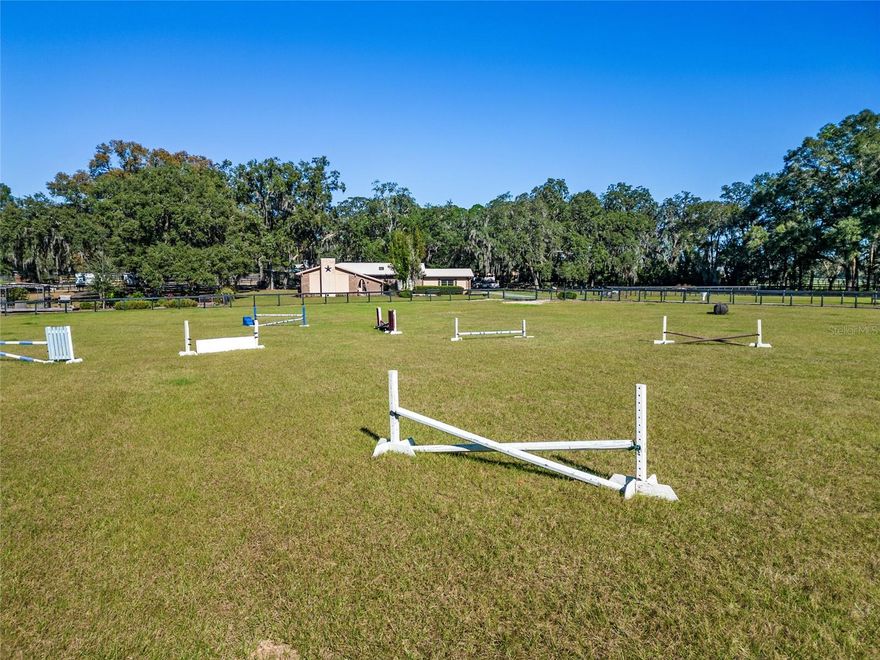 Experience the best of Ocala’s iconic horse country with this refined 10-acre offering, located less than half a mile from the World Equestrian Center and under 15 minutes to both HITS and Ocala Breeders Sales. Blending equestrian functionality with relaxed country elegance, this property presents a rare opportunity in one of the region’s most coveted locations. Fully fenced and gated for privacy and peace of mind, the land is framed by mature oaks and thoughtfully laid out with 14 board-and-wire paddocks, a well-groomed jump field, and a dedicated round pen. Two barns—offering a total of 12 stalls—are equipped with a wash rack, hot water, fly spray system, tack room, and feed room to support daily routines with ease. A spacious workshop and RV garage add further versatility for hands-on hobbies, storage, or extended-stay visitors. Also included is a covered RV with an attached deck, offering an additional inviting space for guests or farm help. A whole-home generator provides added peace of mind. At the heart of the property, a beautifully maintained 3-bedroom, 2-bath home offers over 2,000 square feet of inviting living space. Bamboo wood flooring flows throughout much of the home, complemented by porcelain tile in select areas. A cozy wood-burning fireplace and French doors in the living room open to the back patio, creating seamless indoor-outdoor connection. The kitchen is well-appointed with stainless steel appliances, a gas range, built-in wine rack, breakfast bar, and ample counter space. The expansive primary suite includes its own wood-burning fireplace, an oversized walk-in closet with built-in shelving, and a luxurious private bath complete with soaking tub, walk-in shower, and in-suite laundry. Outdoor living is just as inspired. A screen-enclosed pool area features a sparkling in-ground pool, shaded lounge area, and panoramic views of the surrounding farm. A raised porch with pergola offers a quiet perch above the jump field, while a shaded garden nook and front paver patio provide inviting spaces for gathering or relaxing. Blending thoughtful amenities with timeless charm, this property is an ideal base for active equestrians or those seeking a tranquil, well-appointed retreat. With infrastructure in place and a prime location, it’s ready for your horses, your vision, and your next chapter.