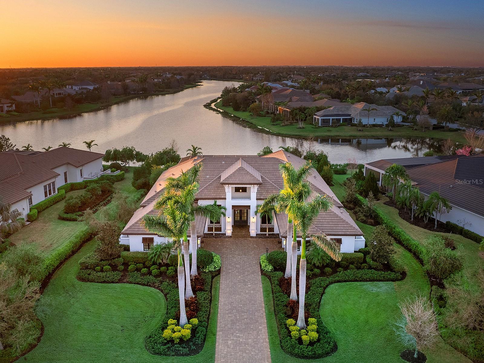 The epitome of luxurious, lakeside living is waiting for you in the exclusive Lake Club at Lakewood Ranch. Looking out over 100 feet of lakefront, this home appreciates amazing long views of the sunset over the water with its northwest exposure in the back. Built to the most exacting standards and filled with elevated finishes, this Clairborne II by Stock Luxury Homes is offered FULLY FURNISHED for the ultimate convenience and is ready to move in NOW! Situated on an oversized lot of 0.60 acres, you’ll enjoy a private retreat surrounded by lush landscaping and towering palms. This open floor plan showcases bright and airy finishes completed by warm and natural tones. The entertaining areas are seamlessly brought together by oak hardwood flooring, 16’ ceilings with custom details and crown molding, designer light fixtures, custom window treatments, Sonos sound system, and large windows and sliders letting in natural light with lake views. The central great room is enhanced by a custom shiplap ceiling and feature wall, built-in display shelving and built-in entertainment center, plus pocketing impact sliding glass doors to the lanai. The chef’s kitchen offers a cozy and functional space with a large central island for guests to gather around, plentiful storage cabinetry with pot and pan drawers, stainless steel appliance suite, stone counters, and large walk-in pantry with shelving. Enjoy formal and holiday meals in the formal dining room complete with a glass feature wall of wine bottle storage display along with a wine refrigerator. Casual weeknight meals are best enjoyed from the dinette nook with large windows overlooking the lake views, or alfresco on the lanai. The expanded paver lanai with classic colonnade screen enclosure highlights the beautiful lake views which can be enjoyed from the covered entertaining space, from the open lanai area, or from the heated saltwater pool and spa. The outdoor living area features beamed ceiling, and a cozy fireplace with stone surround. Enjoy meals prepared at the outdoor kitchen with bar-height island and stainless steel grill in the covered dining area. And there’s no better way to end the day than watching the sunset over the lake from the incredible pool and spa with 360 spill-edge and fire bowls. Inside the primary retreat is smartly located next to the private study with built-in desk and cabinetry, and fitness room with mirrored wall and adjacent powder bathroom, creating an owner’s wing with every convenience imaginable. The spacious bedroom offers a private seating area with lake views, dual walk-in closets with custom shelving, and en-suite spa-like bathroom with a modern freestanding tub, dual vanities, and walk-in shower. Guests will enjoy their own private bedrooms, two of which have private en-suite bathrooms. The 4th guest bedroom has an adjacent full pool bathroom, custom wall detailing, and is large enough to be flexible as a bonus room if desired. Complementing this residence is an oversized laundry with lots of counterspace and storage, an air-conditioned Florida basement storage room, and split 4-car garages with custom built-in storage cabinetry. Peace of mind is secured with impact windows and doors, generator, and quality construction. The Lake Club is an exclusive premier, gated community with a Grande Clubhouse, restaurant, pool, tennis, pickleball and more. Today is the day to make your Florida dream become a reality.