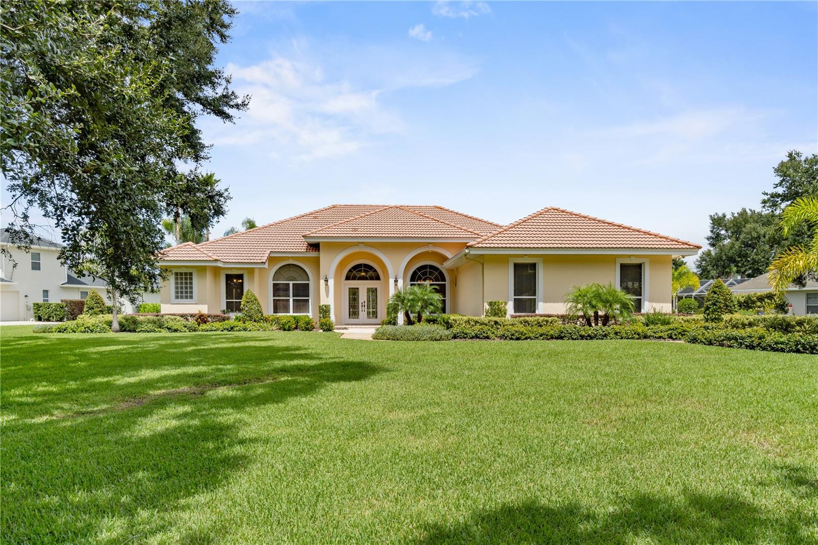 GATED AND GUARDED WATERFRONT PROPERTY – WYNDHAM AT LAKE WINTERSET: Welcome to 105 Wyndham Drive, an extraordinary custom residence within the prestigious gated and guarded community of Wyndham at Lake Winterset. From the moment you arrive, the community sets the tone for elegance and prestige with its brick-paved entry, charming guardhouse, and manicured landscaping that changes with the seasons. Behind the gates, oak-lined streets and impressive executive lots create an enduring setting, where neighbors enjoying leisurely walks and bike rides add to the warmth and charm of daily life. Perfectly positioned on a rare and expansive 0.80-acre waterfront lot, this home offers one of Wyndham’s most breathtaking settings, with tranquil pond views highlighted by a signature fountain. Mature trees, lush landscaping, and a classic tile roof frame the elegant façade and sweeping yard, establishing an immediate sense of sophistication and serenity. Inside, architectural detail meets everyday comfort. The 3-bedroom, 3-bath layout (plus an executive office that can easily serve as a fourth bedroom) offers soaring ceilings, crown moldings, upgraded wood floors, and walls of windows that flood the home with natural light and serene water views. The kitchen blends elegance and function with custom honey-toned cabinetry, dentil crown molding, glass-front display cabinets, a built-in desk nook, richly patterned granite countertops, granite backsplash, and stainless steel appliances. Just off the kitchen, the spacious family room features a cozy fireplace and built-in wine rack—ideal for entertaining or relaxed evenings at home. Whether it’s the elegance of the formal living and dining rooms or the comfort of the family room, each space is crafted for effortless entertaining. The private primary suite is a retreat with space for a sitting area, dual walk-in closets, and a spa-like bath featuring sconce lighting, jetted tub, walk-in shower, and dual sinks. Additional bedrooms are generously sized and thoughtfully separated for privacy, while the executive office with built-ins and a closet offers true flexibility. Step outside to discover the ultimate in Florida outdoor living. A covered lanai with audio and TV connections, expansive paver patios, lagoon-style heated pool and spa, and an outdoor firepit all overlook the sparkling pond and fountain—an idyllic backdrop for both lively entertaining and peaceful relaxation.
The oversized two-car garage, finished with epoxy floors and wall-to-wall storage, easily accommodates vehicles while keeping household items neatly tucked away. Recent updates include new wood flooring in all bedrooms and the office, new tile flooring in the primary and guest baths, expanded patios, upgraded irrigation, fresh landscaping, and new paint inside and out. This intimate lakefront enclave offers tennis/pickleball court, basketball, playground, and secure manned entry—all in a location that combines natural beauty with convenience. Less than an hour from Disney World and 1.5 hours from both Orlando and Tampa international airports, you’ll also enjoy close proximity to Winter Haven’s shopping, dining, medical facilities, and the renowned Chain of Lakes.
Don’t miss this rare opportunity to own one of Wyndham’s finest waterfront properties—a home that combines luxury, privacy, and the irreplaceable beauty of a sprawling 0.80-acre waterfront setting.