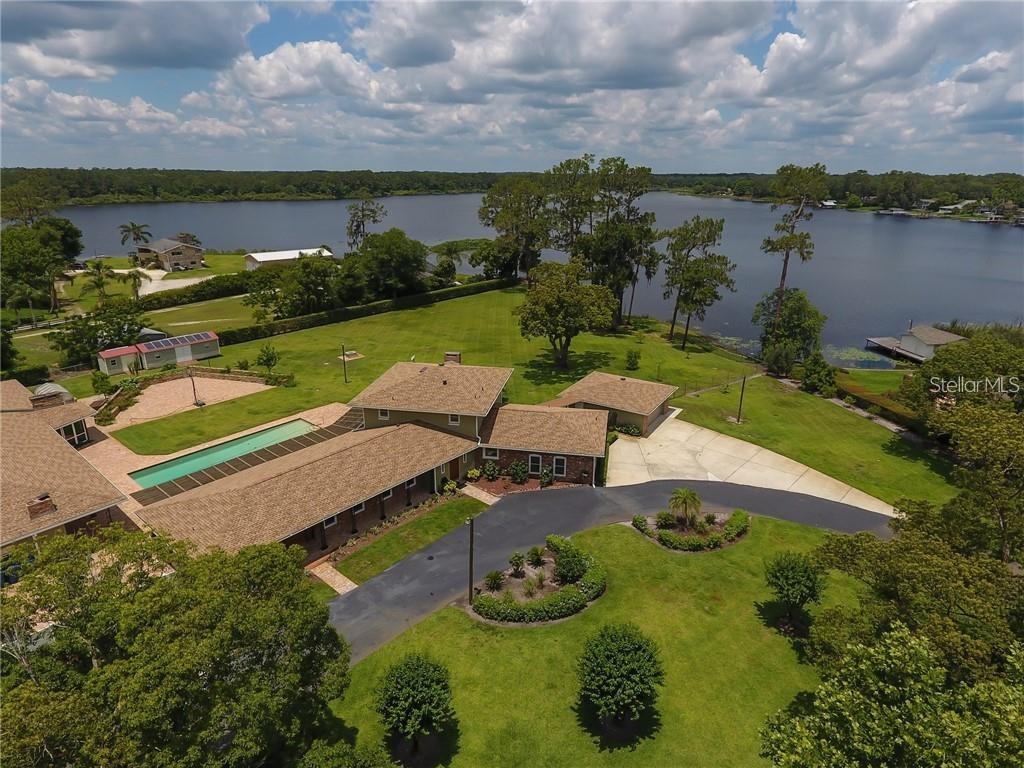 Discover a one of a kind, lake front multi-generational estate! This exceptional property offers a rare blend of privacy, comfort, and versatility. It truly has it all! Set lake front on Lake Talmadge in DeLand on a sprawling 2.65 acres, featuring a spacious main home, two fully equipped in-law residences, 2 garages, a pool, amazing views, and more! The main home features 3 bedrooms with 3 full en-suite bathrooms and powder room, a gourmet kitchen, butlers pantry, 2 fireplaces and more. The unique qualities are evident from the moment you step through the grand carved oak doors. Chicago brick paves your way through the foyer to the massive great room, featuring luxury vinyl flooring, custom crown molding, and walls of windows. Designed for both the aspiring home chef and effortless entertaining, at the very heart of the home, the gourmet kitchen is as functional as it is breathtaking. Featuring high-end stainless steel appliances, custom cabinetry, Brazilian granite, gas range with pot filler. The open layout flows seamlessly into the surrounding living and dining areas, while the wood burning fireplace and lakefront views create a backdrop of natural beauty while you cook, dine, or entertain. Adding to the homes functionality, is a thoughtfully designed butlers pantry complete with custom cabinetry, stainless steel sink, granite counters, and a huge walk-in pantry. Retreat to the expansive upstairs primary bedroom, a serene retreat designed for both luxury and relaxation. Enjoy breathtaking views while a wood burning fireplace adds warmth and charm. The suite also features 2 custom closets and a luxurious en-suite bathroom complete with soaking tub, shower, and double vanity. The primary home also includes 2 downstairs bedrooms with 2 full en-suite bathrooms, and indoor laundry room, and a 24x26 garage. Primary home updates and features include Roof 2018, HVAC 2015, Tank less W/H 2015, updated Electric 2015, FAS Windows 2024. Adding to its exceptional versatility, the estate also includes two fully equipped in-law homes. Thoughtfully designed, each in-law home includes 1 bedroom, 1 full bathroom, fully updated kitchens, private entrances and beautiful pool and lake front views. The in-law homes provide privacy, comfort and modern conveniences to family and guests. Updates and features to the in-law residences include, Roof 2018, New Mini Splits, Tank-less W/H 2015, Updated electric 2015, FAS Windows 2024, custom closets and cabinetry, 1- wood burning fireplace, 1 -24x25 garage with W/D hook up and new ceiling. Step outside and experience the true beauty of this lakefront estate’s outdoor living space. The expansive grounds feature paved raised garden beds, as well as a dedicated greenhouse for year-round cultivation. Surrounding the property, you’ll find a variety of mature fruit trees that provide abundance and charm. At the center of it all is a sparkling 50x20 pool with unobstructed views of the lake, creating a resort-like atmosphere and true outdoor Florida lifestyle. Exterior property updates include: Gas Powered home Generator, Property Reverse Osmosis Water Filtration System, New Pool pump 2023, New Well Pump 2023, 3 septic tanks, 500 gallon LP tank underground, Resealed driveway 2025, Exterior Paint 2025, Fully Fenced, 12x30 shed and 8x12. This property is a rare offering that has it all! Take the opportunity to own your multi-generational paradise and schedule your showing today.