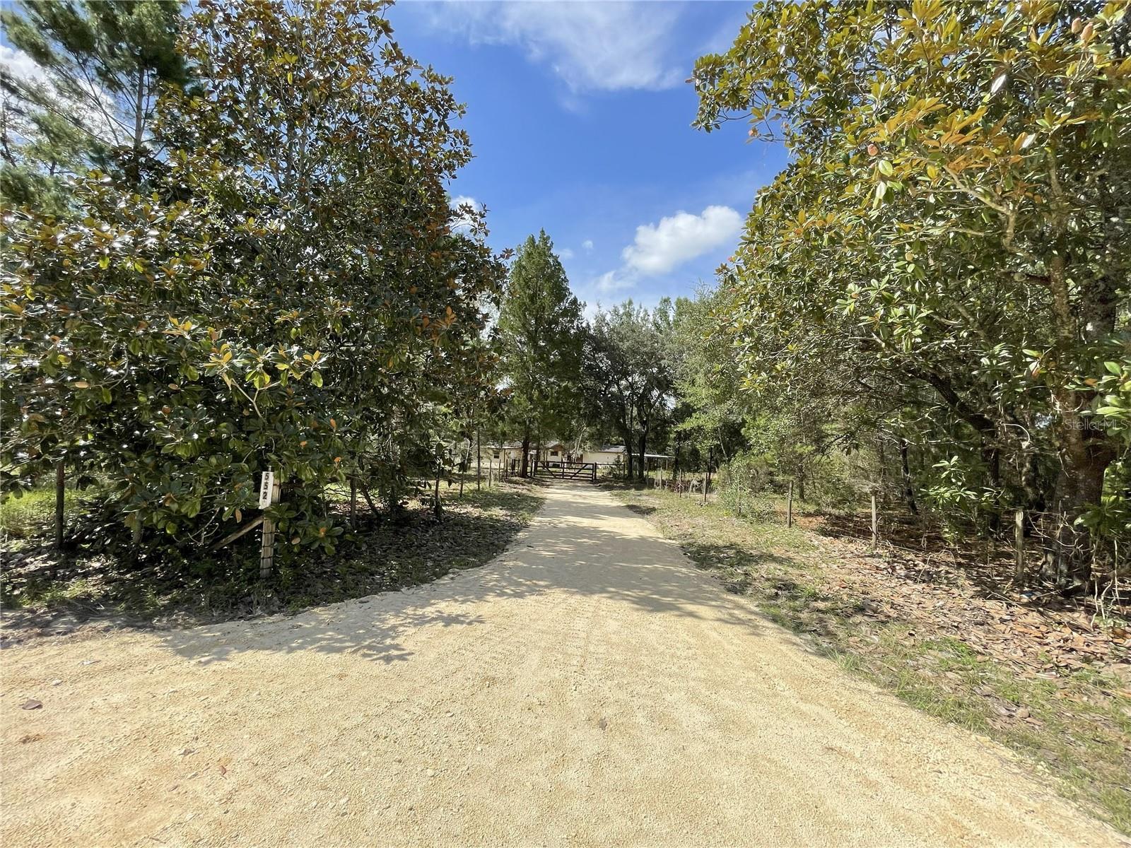 2.64 Wooded Acres in Wonderful Dunnellon -
Escape to your private wooded retreat in Dunnellon! Located on 2.64 acres, this gated and fenced property offers a peaceful and serene environment, surrounded by nature. The 3-bedroom, 2-bathroom manufactured home is in need of some TLC but is fully livable, providing an excellent opportunity for your dream get-away in the woods.
Several outbuildings on the property include a spacious workshop/garage, perfect for hobbyists, DIY projects, or extra storage. A standalone laundry facility adds to the convenience. The property also boasts a functioning well, septic, and electricity ensuring self-sufficiency in this tranquil location. Private entry gate. Complete fencing on all four sides of the property.
The brand new lime rock driveway has just been re-graded and finished, and the inviting entryway is beautifully flanked by two majestic Magnolia trees. With nicely paved access roads, this home is just a short commute to the stunning Rainbow River and only 20 minutes from the Suncoast Parkway, offering exceptional convenience and easy access to nearby amenities.
Whether you are seeking a peaceful retreat, room to grow, or the chance to create a home and property tailored to your tastes and your lifestyle, this property provides the perfect canvas. Do not miss the opportunity to own this private and wooded oasis!