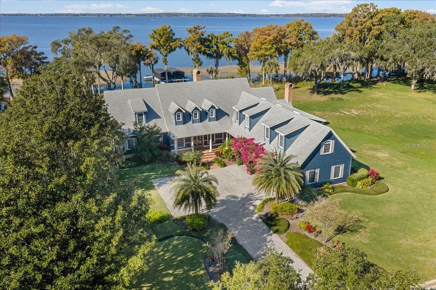 Welcome to an extraordinary lakefront estate in Tavares, gracefully positioned on a private peninsula along the coveted Harris Chain of Lakes. This exclusive enclave of 17 parcels is the most sought after address in Tavares.  Encompassing 6,288 square feet, this timeless Cape Cod-style residence, built in 1997, blends classic architectural charm with expansive living spaces and an unparalleled waterfront lifestyle.  This .9-acre home site sits at the water’s edge dotted with stately cypress trees. The sunsets are spectacular year-round and no two are alike!
Boasting 5 bedrooms, 4 full baths, and 2 half baths, this thoughtfully designed 6,288 square foot  home offers both elegance and functionality. The main level features a spacious primary suite, providing privacy and convenience, while rich wood floors and a stunning double-sided gas fireplace create warmth and sophistication throughout the living areas.
At the heart of the home, an inviting eat-in kitchen flows seamlessly into the family room, where vaulted ceilings with tongue-and-groove detailing and a cozy fireplace create an ideal gathering space.  This open-air kitchen offers a connection to the family room, kitchen dining area, and family room with vast water views of Lake Harris. Upstairs, three additional bedrooms and two full baths provide comfortable accommodations, while a separate oversized bunk room above the garage offers the perfect retreat for small guests. An additional private suite above the garage—complete with its own living room, bedroom, and full bath—adds flexibility for multi-generational living or extended stays.
Designed for effortless indoor-outdoor living, the expansive covered brick lanai is a true showpiece. Complete with a gas firepit, built-in grill station, and dedicated dining area, this space is perfect for entertaining while enjoying serene lake views and unforgettable sunsets. This covered lanai creates an abundant space for luxury dining and entertaining by the water. 
Step outside to a resort-style setting designed for both relaxation and entertaining. A free-form in-ground pool creates a private oasis, perfectly complemented by the expansive covered brick lanai.  Surrounded by lush landscaping and serene water views, this outdoor space captures the essence of Florida luxury living—ideal for hosting or unwinding poolside as the sun sets over the lake.
A lighted paver path leads to the covered boathouse featuring 2 boat slips with automated covers and electric lifts.  This is a premium, ShoreStation dock and boat lift system which enhances the waterfront experience, offering durability, convenience, and immediate access to the Chain. With direct entry to the Harris Chain of Lakes, enjoy world-class boating, fishing, and waterfront dining right from your backyard.
Live like you are on vacation with the 15,088-acre Lake Harris as your backyard or explore the 75,000+ acres of the Harris Chain of Lakes, offering old Florida scenery, waterfront dining options, and quaint, walkable downtowns. In approximately 10 minutes by boat, you can arrive at downtown Tavares, "America's Seaplane City," or the charming historic streets of Mount Dora, celebrated for its exceptional dining, boutique shopping, and year-round festivals. A rare offering where refined design meets relaxed waterfront living—this is lakefront luxury at its finest!  See you at sunset!