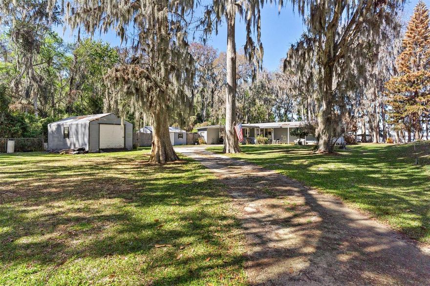 Affordable Chain of Lakes Living – Private Lake Harris Waterfront with Endless Possibilities. If you’ve ever imagined what “Old Florida” truly feels like, this property brings that vision to life. As you turn onto the quiet road leading to the home, you’re welcomed by a natural canopy of towering cypress & oak trees draped in Spanish moss, the sunlight filtering gently through the branches. The drive sets the tone for what awaits ahead—a hidden waterfront retreat where the pace slows down & nature takes center stage. With only 3 homes on the street, privacy and tranquility surround you from the moment you arrive. Situated on just under an acre of land, this property captures the charm & authenticity of classic Fl lakefront living. The shoreline is lined w/ majestic cypress trees rising from the water’s edge, their reflections dancing across the lake, while birds glide overhead & the gentle breeze carries the sound of nature around you. It’s the kind of place where mornings begin w/ coffee by the water & evenings end w/ lakefront sunsets. The best part—you own the land & there is NO HOA! Located directly on Lake Harris, part of the renowned Harris Chain of Lakes, you’ll have access to miles of interconnected waterways perfect for boating, fishing, sunset cruises, & exploring waterfront restaurants across the chain. Walk down toward the lake-a perfect starting point for days spent out on the water. Shaded by mature trees that create the perfect blend of privacy & natural beauty. Whether enjoying the peaceful backyard, relaxing in a hammock under the trees, or hosting friends for a lakeside gathering, the outdoor setting truly defines the lifestyle this home offers. Inside, this 2/2 provides a comfortable & welcoming layout. A 2-car carport greets you as you arrive & leads you into the kitchen & breakfast nook. Down the hall you’ll find the guest bedroom & guest bath featuring a tub/shower combination, while the primary bedroom suite offers 2 closets—including a walk-in—& a private bathroom w/ walk-in shower. The oversized family rm flows seamlessly into the dining area, creating an open & inviting space for gathering w/ family & friends. Large windows allow natural light to fill the home, while offering glimpses of the beautiful outdoor setting. One of the most enjoyable spaces is the Fl Room, where large windows & sliding doors frame views of the backyard & Lake Harris beyond. While not under heat & air, it could be the perfect place to relax w/ a book, watch the wildlife, or enjoy peaceful waterfront scenery year-round. Need extra storage? You’ll love the huge utility room, providing plenty of space for hobbies or additional storage. Did I mention there is also 2 sheds in the front yard. The property also features a large screened lanai, offering the perfect place to sit back, enjoy the breeze off the lake, and take in the peaceful surroundings. Recent updates include:• Roof – approx 8 years old• A/C – approx 3 years old• Hot Water Heater – approx 4 years old• Newer appliances. This property offers the flexibility & opportunity that so many buyers are searching for. Whether you’re looking for a weekend lake escape, a seasonal Fl retreat to leave the snow behind, or a place to enjoy now while planning your future custom waterfront dream home, this property delivers.Opportunities like this—are becoming increasingly rare. Come experience the charm, privacy, & timeless beauty of Old Fl lakefront living. Your waterfront dream begins here.