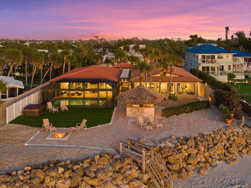 Immerse yourself in the pinnacle of beachfront living along Manasota Key with a renovated home that has it all for entertaining, TURNKEY furnished, private living space for the owners, separate space for guests, a large pool, hot tub, tiki bar, outdoor kitchen, sunken fire pit and a wide beach. The experience begins along the journey of a paver tile driveway which leads to an extraordinary home along the beach. Nestled on almost half an acre and surrounded by low-maintenance tropical landscaping, lies a beachfront get-away meticulously renovated with the intent to create a playground for entertaining. Upon entering, prepare to be captivated by the courtyard that provides a feeling that an experience is around the corner. The courtyard creates privacy that separates the home from the owners and the guests, and it features a pergola ceiling with smart technology and sensors with the ability to control the sun and rain. The owner’s wing features a gorgeous kitchen, a living room with a linear fireplace and decorative built-ins, a primary bedroom with an ensuite bath, an office/den, guest bathroom, large laundry room for additional storage, and a 2-car garage with epoxy flooring and room for storage. The kitchen is the heart of the home and features quartz countertops, stainless steel appliances, white cabinetry with upper glass inserts, and a large island with seating for eight people. The guest wing features three additional bedrooms, two bathrooms, and a living room with finishes of comfort. The living room features a full kitchenette, an entertainers’ bar where stories unfold, and a linear fireplace with built-ins. The home presents with a tile roof, impact windows and doors, terrazzo and tile floors throughout; all for peace of mind and easy maintenance. This home blurs the lines of indoor/outdoor space with walls of beach facing sliding doors that open to the outdoors. The interior of the home is beautiful and unique; however, the outdoor space provides a feeling that you arrived at a destination that sets the tone to utilize the space for relaxation and provides a venue to be proud of for entertaining family and friends. Earth, air, fire and water are elements that will calm the soul in this outdoor playground. 100’ along the beach is the crown jewel of this home. Walk a few steps towards the water to realize full appreciation of the wide beach that presents for pure enjoyment. Substantial riprap has been carefully placed for protection and stabilization. The screened area includes covered spaces for outdoor living, a large pool and a clear-view screen for a mesmerizing view. Imagine sharing stories with kindred spirits at the tiki bar while grilling the day’s catch at the thatched tiki bar. As the sun begins to set a nightly work of art appears in the sky with colorful sunsets over the Gulf of Mexico. A sunken fire pit along the beach beacons those who desire a mesmerizing experience. The outdoor space has been thoughtfully designed to be low maintenance as well as a tropical setting featuring a large concrete patio lined with lighted edging and artificial grass. This beachfront home includes Bay easement with a shared dock for an additional element of waterfront living. Lively restaurants and entertainment are located within a 5-minute drive. Acquaint yourself with this home by scheduling a private showing.  Copy and paste the following link to view the Luxury Video https://iframe.videodelivery.net/98882b57f46056c72064a754202ce185