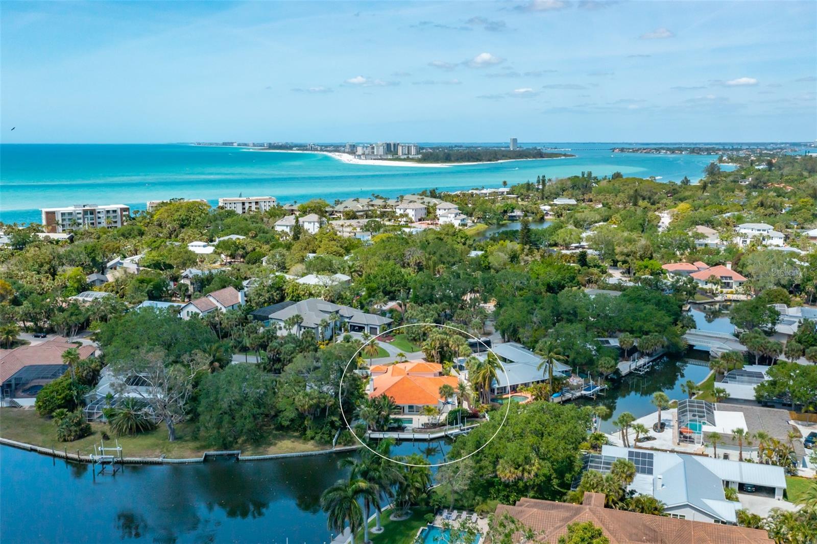 Live the dream in this delightful island home with broad water views along a T-shaped canal and
the tropical splendor of Siesta Key. Exquisite waterfront living envelops this Spanish-influenced home that lures you to enjoy even more water pleasures with a 10,000 lb. boat lift on the east that will never obstruct views. 125 ft of canal frontage creates a tranquil canvas for living. Magazine-worthy renovations means the four-bedroom, four-bath residence lives like new construction. An extensive pavered circular driveway and parking pad for the three-car garage greets your approach as you stroll through the wrought-iron gate past the pineapple fountain in the courtyard. Travertine walkways wrap around the home and lead to the large open portico and pool area. Entering through the Mexican double wooden doors into the foyer, you can see through the expansive open floor plan to the pool and beyond to the canal. Imbued with a coastal color palette, natural light brightens the open space featuring an eye-catching cathedral ceiling and a carved stone fireplace. The sparkling white kitchen boasts Cambria quartz countertops, stainless Thermador appliances, and a beautifully designed island with seating for four. A separate living room off the main space is perfect for good conversation or family movie night under the vaulted ceiling. Engineered hardwood floors connect and unify all main areas of the home. The outdoors is a cherished feature with one or more sets of sliding glass doors in every main room. The renovated primary bedroom suite offers a large luxury bath with a door to the pool deck and walk-in pass-through closet. Step out through the bedroom’s sliding glass doors onto the portico for a late afternoon swim. The open-air portico feels like a Mediterranean getaway that houses an outdoor living room under roof and seamlessly transitions to the pool deck, pool, outdoor dining, dock, and walkway to the boat lift. Entering from the unique garage foyer, you can step into a lovely private guest suite with full bath as well as the den/office with a vaulted ceiling. Located near what has been named the No. 1 beach in the nation, this home is within walking distance of Siesta Village and its robust restaurant scene and is just over the bridge from the heart of Sarasota – known for its dynamic arts and culture scene, beautiful golf courses, and bustling waterfront downtown.