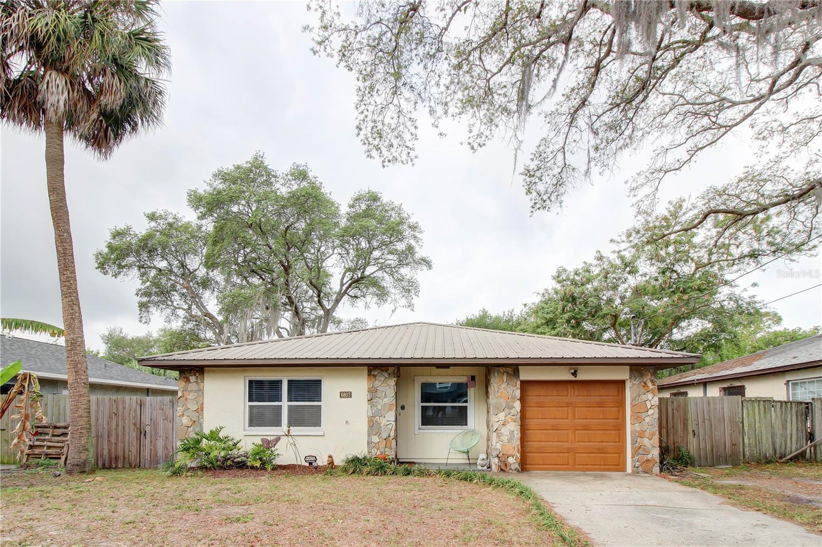 One or more photo(s) has been virtually staged. Located in highly desirable South Tampa, this recently updated and freshly painted 3-bedroom, 2-bathroom home with a 1-car garage offers approximately 1,496 square feet of comfortable living space. Its prime location near MacDill Air Force Base and Gadsden Park makes it an ideal home for military personnel, families, or anyone seeking convenience, recreation. Inside, the home features an open floor plan with a spacious living room, a dedicated eating area, and a cozy sitting space by the front window. The kitchen is well-appointed with stainless steel appliances, including a flat-top range, dishwasher, and refrigerator. It also features a breakfast bar and a range hood that vents directly to the outside, as do the fans in both bathrooms. For a clean, modern look, the switches to the range hood and dishwasher are cleverly hidden. Dimmer switches have been installed for all lighting not connected to ceiling fans, allowing you to control the ambiance throughout the home. The primary bedroom includes a remodeled en-suite bath featuring classic subway tile and a honed marble mosaic shower floor. The bathroom exhaust fan offers Bluetooth capability for playing music and includes a blue night light feature and updated flat panel LED lights. All bedrooms are fitted with new matching ceiling fans, while the living room boasts a large, high-end ceiling fan. All entry doors in the home have been upgraded, including a hurricane-rated, insulated garage door with a beautiful finish that complements the custom fiberglass front door. The door between the kitchen and garage is fire-rated for added safety. An automatic garage door opener and exterior keypad add convenience, while the storm door offers the option to replace the glass panel with a screen mesh to allow fresh air to flow through the home. Flooring includes porcelain tile in all bedrooms and ceramic tile throughout the rest of the home. Outside into a large, fenced backyard — perfect for outdoor gatherings, pets, or simply relaxing. This home is located just minutes from MacDill AFB, downtown Tampa, the bridges to Pinellas County’s stunning beaches, and the restaurants and shops of South Tampa. This move-in-ready home offers the perfect blend of comfort, functionality, and location. Schedule your showing today