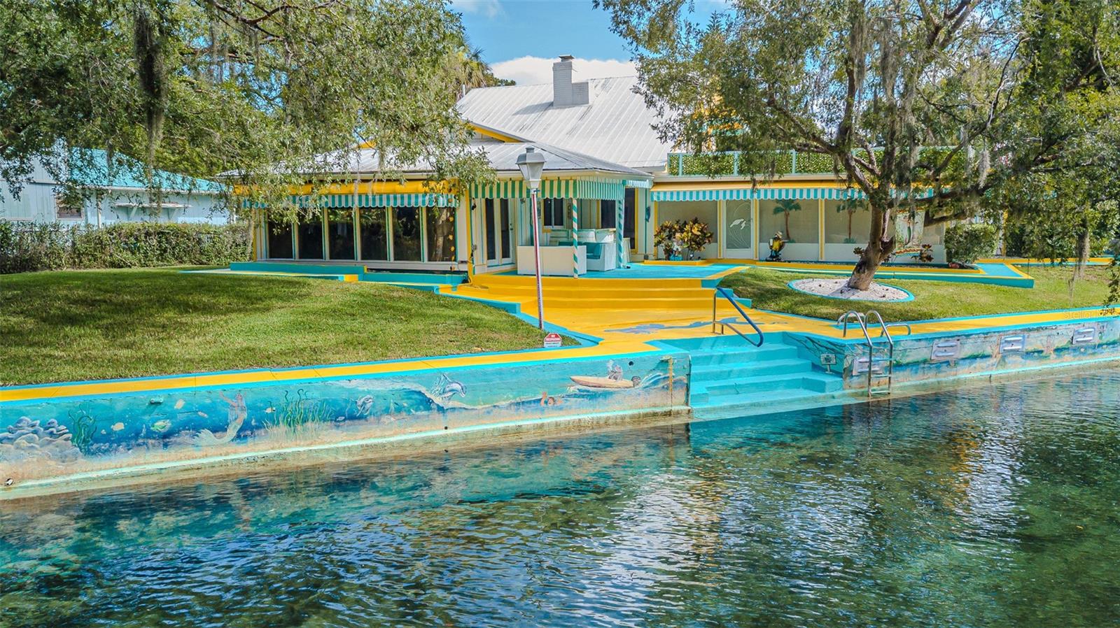 Welcome to this incredibly rare opportunity to own this ICONIC RIVERFRONT PARADISE RETREAT, this is truly a gem that offers a nostalgic journey into old Florida that invites you to experience the best of outdoor living. This residence was formerly known as "Pam's Mermaid House." It is located on the Main & Wide Part of the Weeki Wachee River, a 7.5 mile long waterway of spring-fed beauty that leads out into the Gulf and the home has NEVER BEEN FLOODED! Those navigating the waterways have been awed by the colorful paintings of sea creatures that wrap around the magnificent large 145'+ seawall. The home itself is ablaze with colors of yellow and turquoise set off by the beautiful, striped awnings, concrete walkways around the entire home & it is surrounded by a beautiful mature landscape, trees & bushes. This meticulously maintained custom home offers the perfect blend of charm with an abundance of many details throughout and functionality. Indulge in the enchantment of this vacation-like waterfront residence that offers breathtaking views of the crystal-clear waters of the Main River, stunning scenery and surrounding preserve. This Waterfront Retreat may also be utilized as an elite VRBO or AIRBNB. The owner previously rented out 1/2 of the house while living in the other 1/2 of the home. Entering the property through the gate, you will be greeted by the beautiful turquoise & yellow driveway and tastefully landscaped front yard. The entrance foyer has a hardwood floor & 3 huge etched glass windows of a Mermaid, Captain and Manatee. This is a move-in ready property that features 3 bedrooms, 2 full bathrooms, central air conditioned 2 car garage, a large great room, dining room, living room with a wood burning fireplace, large open-air screened Florida room, sitting area, & indoor laundry room. Tile floors throughout the home except for carpet on the stairway & primary bedroom. Upon entering off the main foyer, you'll be captivated by the soaring vaulted ceiling, an open-concept layout & an abundance of natural light. Your main area features the kitchen, dining room, living room with a step down into the great room, and a FULL PANORAMIC VIEW of the river, with massive glass doors and windows throughout. The 2nd story consists of the private oasis of the primary bedroom and ensuite bathroom with a jetted spa tub. From the bedroom you can use the sliding glass doors to enter outside on to the large private rooftop and enjoy your cup of coffee in the morning and view the stunning crystal-clear waters while soaking in the beauty & tranquility of waterfront living & you'll have no neighbors across the river except for the wildlife preserve! City water is not used for the irrigation system, it draws from the river. Minutes from beaches, shops, and restaurants, this home is in a PRIME LOCATION. Launch your kayaks, go swimming or fish right in your backyard and just enjoy all the Weeki Wachee Spring has for you from manatees to dolphins for truly a unique experience. You have so many choices of fun & exciting things to enjoy such as the Weeki Wachee State Park with the live Mermaid shows that have been a roadside attraction since the 1940's where visitors have marveled at live performances in an underwater theater & amusement rides, Buccaneer Bay Water Park & Pine Island on the Gulf of America. This home is fully fenced so bring your furry friends. Call today to make this paradise a reality before it's gone! LOCATION! LOCATION! LOCATION!