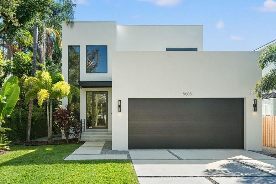 Tucked away in a private enclave, this property ensures your privacy without sacrificing convenience or luxury. Just steps from stunning bayshore views, this meticulously crafted 2,815 sq. ft. home seamlessly blends modern sophistication with everyday comfort. Constructed like a fortress with masonry exterior walls on both the first and second floors, this home sustained no damage or water intrusion during last year’s hurricanes. As you enter through a grand 20' ceiling foyer, expansive commercial ‘impact-rated’ doors and windows flood the open-concept interior with natural light, showcasing sleek, high-end finishes. The kitchen, a standout feature, spans the length of the home, featuring a 10 ft quartz waterfall island perfect for entertaining, a seamless bar flowing into the dining area, and views of the entire floor, including the expansive outdoor balcony that stretches across the back of the home. Adjacent to the balcony, an outdoor kitchen elevates the space, complete with a built-in grill, sleek countertops, a stainless steel sink, and ample storage, perfect for hosting gatherings. The living room radiates sophistication with a three-sided electric fireplace, creating a warm ambiance for cozy evenings. Imported Italian 48 x 48 tiles flow throughout the first floor, enhancing the seamless indoor-outdoor living experience. An additional feature showcases a 135-bottle wine rack display encased in floor-to-ceiling glass, accented by satin-finish handlebars. Additional conveniences include a walk-in pantry, powder bath and a discreet hidden closet for private storage. The first floor also features a spacious two-car garage with an epoxy-coated floor, complemented by stairs with the same imported Italian tiles as the home’s interior, ensuring a cohesive and luxurious aesthetic. Upstairs, lush tropical landscaping with towering palms and meticulously manicured grounds captivates the senses. This three-bedroom home offers intimate spaces for relaxation, with the primary suite serving as a tranquil retreat. Its windows frame mature trees, creating a serene, treehouse-like ambiance as you feel suspended among them. The suite flows effortlessly into a spa-inspired bathroom, connected to his-and-hers closets and a conveniently accessible laundry room. Thoughtfully crafted for style and functionality, this home is a luxurious haven you’ll never want to leave.