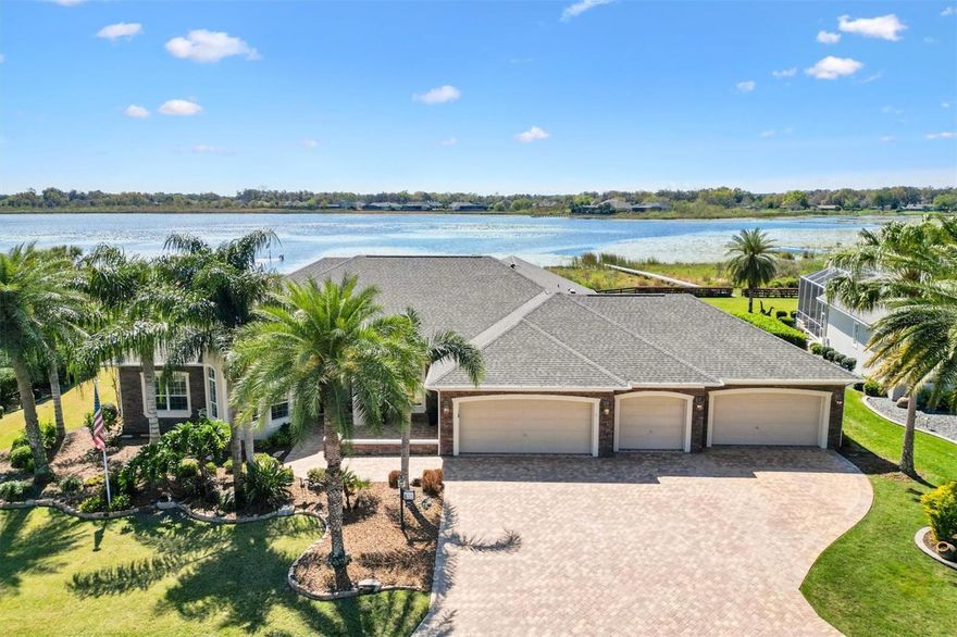 Nestled along the tranquil shores of Lake Miona in the desirable Village of Bridgeport at Miona Shores, this Grandview Premier home is a true masterpiece of luxury and design. Built-in 2009, this 5-bedroom, 2.5-bath estate spans an impressive 4,025 sq. ft. under air (6,448 sq. ft. total) and offers breathtaking water views from nearly every room. A private dock and an expansive 34’x18’ pool with a screened enclosure, full summer kitchen, and bar make this home a rare gem for those who appreciate waterfront living at its finest. From the moment you arrive, the paver driveway, walkway, and grand double-door entry welcome you into a space where elegance meets functionality. Towering 12-foot ceilings enhance the open and airy feel, while the spacious entertaining kitchen features stainless steel appliances, a center island, a breakfast area, and panoramic lake views. A butler’s pantry, complete with a sink, bar fridge, and ample storage, conveniently connects the kitchen to the formal dining room. The den, positioned between the kitchen and primary suite, offers a cozy retreat with stunning pool and lake views, highlighted by a tray ceiling for added elegance. The Primary Suite is a true sanctuary, featuring a French door entry, tray ceiling, two walk-in closets, and a spa-like ensuite with a Roman shower, soaking tub, dual vanities with granite countertops, a private water closet, and an additional storage closet. The guest wing provides privacy and comfort, with two spacious bedrooms sharing a well-appointed bath. The rear guest bedroom boasts exceptional pool and lake views, enhanced by exterior sliding doors. A fifth bedroom addition, complete with its lanai, transom windows, and closet, offers endless possibilities as a guest suite, media room, etc. Designed for both luxury and practicality, the oversized 3-car garage + 2 golf cart garages (1,358 sq. ft.) includes workshop space, cabinetry, and a Magic Stairs system with a Dumbwaiter leading to a decked attic for additional storage. The home is further enhanced by a new roof in January 2025 and two HVAC units, with Unit 2 replaced in November 2024.