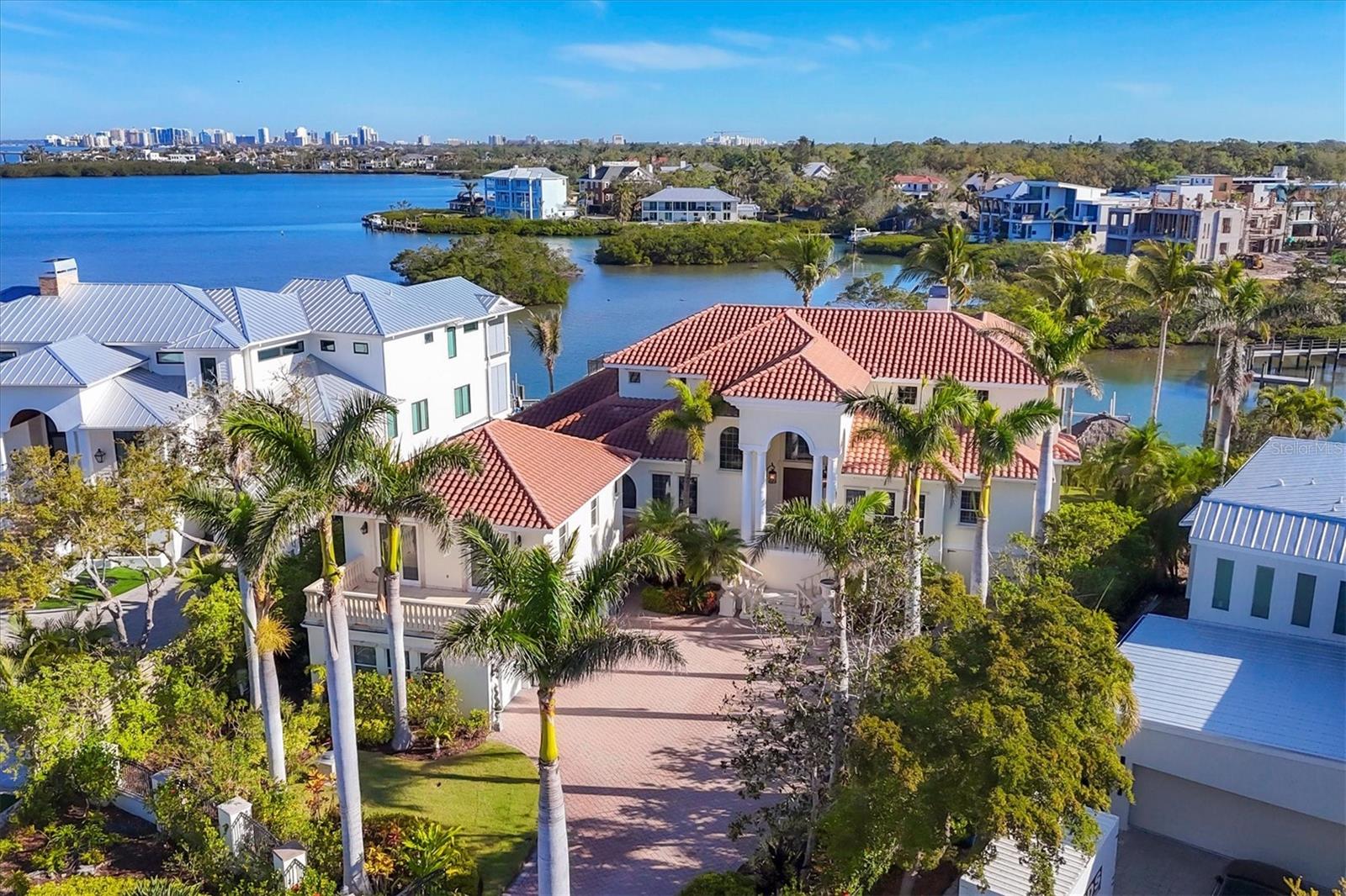 Located West-of-Trail in one of Sarasota’s sought-after neighborhoods, Oyster Bay Estates, this stunning waterfront home is designed for those who appreciate breathtaking views and effortless entertaining. With a prime position on Sarasota Bay, this gated estate captures panoramic vistas of the city skyline, preserve and mangrove islands, and beyond. Blending timeless elegance with modern comforts, the home offers seamless indoor-outdoor living, quality finishes and thoughtfully designed spaces. A grand entrance sets the stage, with travertine stairs leading to stately double doors completed by a transom arch window. Inside, the living and dining areas boast a detailed coffered ceiling framed by a wall of sliders that showcase uninterrupted water views. A gas fireplace with a carved stone mantle anchors the space while custom wood shelving, wainscoting-lined hallways and artisanal millwork accentuate timeless craftsmanship. For culinary enthusiasts, the gourmet kitchen is functional and luxurious. Anchored by an oversized central island with a prep sink, it offers abundant workspace, granite countertops and custom wood cabinetry. A top-of-the-line Viking® appliance package pairs seamlessly with a Sub-Zero professional-grade refrigerator, while a deep basin sink and a spacious walk-in pantry with custom organization enhance convenience. An adjoining butler’s pantry elevates the space with glass-faced cabinetry, a beverage cooler and dishwasher drawers. The casual dining area is positioned to take in breathtaking water views, making every meal a scenic experience. The expansive great room boasts windows that capture views of mangrove islands, city lights and the tranquil waters beyond. Multiple bar areas, each equipped with beverage coolers, prep sinks, dishwasher drawers and granite countertops, ensure effortless entertaining. Retreat to the primary suite, a private sanctuary with a custom tray ceiling, a designer chandelier and bay windows that invite the amazing view in. The spa-inspired en-suite bath features travertine tile, dual vanities, a spacious walk-in shower with multiple showerheads, a jetted tub and an expansive custom-organized closet. A gracefully curved wood staircase ascends to the upper level, where four additional en-suite guest rooms offer luxurious accommodations, most with private balconies that frame breathtaking views. A three-stop elevator provides easy access across all levels. Ideal for large-scale entertaining, the home features a ground-level bonus area, storage and workshop, opening to the resort-style pool deck for seamless indoor-outdoor living. A private guest apartment, accessible via a separate staircase and above the garage, provides a serene retreat with a living room kitchenette, a spacious bedroom, a full bath and a private balcony. This estate has been thoughtfully crafted for elegance and entertainment, featuring Brazilian cherrywood floors, custom-trimmed doorways, wainscoting accent walls, crown molding, plantation shutters, custom-designed coffered and tray ceilings, and a central vacuum system, among other fine details. With stunning water vistas as its backdrop, this is more than just a home, it is a lifestyle conveniently near The Field Club, Southside Village and downtown Sarasota.
