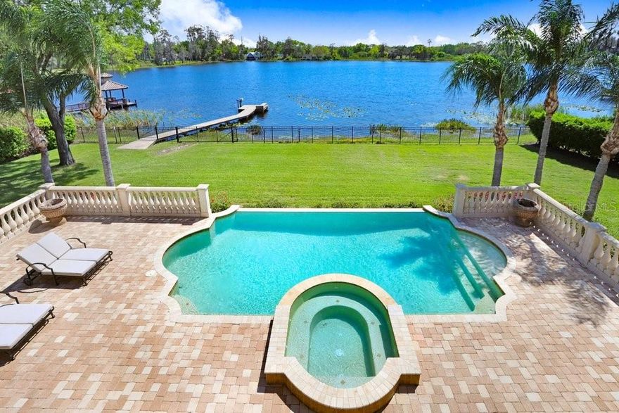 Nestled in the exclusive gated community of Keystone Shores, this exquisite custom-built Mediterranean masterpiece offers unparalleled luxury and stunning lakefront living. Boasting 5 bedrooms, 5 full baths, a powder room, pool bath, office, bonus room, media room, and a 4-car garage, this home spans an impressive 0.81-acre premium homesite with direct access to Little Lake. The serene location, sprawling lawn, and fully fenced backyard make this property an entertainer’s dream. As you approach the home, the captivating curb appeal draws you in with its elegant Mediterranean architecture. Upon entering through the grand foyer, you are immediately welcomed by a sweeping staircase with wrought iron balusters and decorative details. The open layout features soaring vaulted ceilings that flood the space with natural light, creating a welcoming and expansive atmosphere. The formal dining room and living area are thoughtfully separated for privacy and offer a perfect setting for both intimate gatherings and grand celebrations. The heart of this home lies in the stunning, custom kitchen that will delight any chef. Featuring beautiful wood cabinetry, a large center island with a seamless solid piece of exotic granite, and top-of-the-line appliances, including a Wolf 6-burner gas range with griddle, a Sub-Zero fridge/freezer, and a vented hood, this kitchen is a culinary masterpiece. A large dinette area with breathtaking lake views provides the ideal space to start your day. The spacious family room, with its soaring ceilings, polished travertine tile floors, and triple-pocket sliders that open directly to the pool, is perfect for relaxing or entertaining. The sumptuous first-floor master suite is a true retreat, featuring hand-scraped hardwood floors and a deluxe master bathroom that includes dual sinks, a make-up counter, a jetted garden tub, a large frameless walk-in shower, and a “Sarah Jessica Parker” style dual custom walk-in closets that will captivate anyone with its size and organization. In addition to the master suite, the first floor also offers a comfortable office with plantation shutters, a large laundry room with ample storage, and a guest bedroom (or gym) with an adjacent full bath. Upstairs, access one of two staircases to find three spacious en-suite secondary bedrooms, a large bonus room with a fridge, freezer, dishwasher, bar, and plenty of cabinetry, along with a covered balcony featuring a fireplace that offers incredible views of the lake. Adjacent to the bonus room is a custom-designed media room with a projector screen and media center closet, perfect for movie nights or entertaining guests. Step outside into the entertainer’s paradise, where the expansive brick-paved patio leads to an infinity-edge pool and spa. The fully fenced backyard provides privacy and includes direct lake access from your private dock, ideal for fishing or taking in the beauty of the tranquil surroundings. Picture-perfect views reminiscent of On Golden Pond complete this incredible outdoor space. This exceptional property is centrally located in the heart of Odessa, with easy access to great schools, Citrus Park Mall, International Plaza, Tampa International Airport, and more. This move-in-ready gem is truly a rare find, offering a lifestyle of luxury, comfort, and unforgettable memories. Schedule your private showing today and experience this one-of-a-kind lakefront estate firsthand.