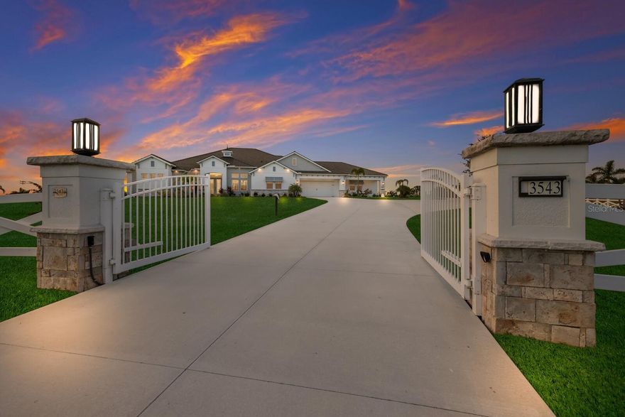 Situated on 8.7 fenced acres with breathtakingly expansive vistas at every turn, this meticulously customized Grand Cayman residence with a modern flair is perched atop stunning grounds within the community of Hampton Lakes. Beyond its private double gates and past the impressive drive reveals an exquisite property completed in 2021 by Medallion Homes showcasing 4,242 square feet of open one-story living with generously proportioned spaces, smart house automation, and a vast outdoor sanctuary. With an expanded roof line well beyond the builder’s original plan, this home’s outdoors delivers a sprawling lanai with abundant under cover space, gathering area with fireplace, full summer kitchen & bar, retractable screens, separate pool deck fire pit, an inviting 65-foot newly resurfaced heated saltwater pool/spa with water bowls, and a roof top observation terrace that swoons all the senses. Seamlessly connecting the resort-styled oasis are impact glass sliders into the oversized living and great rooms each with fireplaces and centered by a showstopper tempered glass-enclosed wine room and a gourmand’s kitchen where chefs will delight in sprawling quartz counters, well-appointed appliances including a built-in Miele coffee maker, and a multi-function concept for pantry, laundry and mud room needs. Dinner guests are treated to tranquil views of the stunning grounds from the oversized island, formal dining room and intimate breakfast nook. Relax and unwind in the elegant owner’s retreat positioned on its own private wing behind double French doors, offering direct lanai access, automated privacy screens, massive walk-in customized closet with island, and a luxurious spa-like bath with dual vanity station, stand-alone shower, and a free-standing soaking tub. Meanwhile, overnight visitors will be right at home in the additional three generous guest suites all with walk-in closets and direct ensuite full bath access. Other highlights of this 6,775 total square foot residence includes a private office/study behind double doors, detached outdoor structure ideal as an exercise or hobby room, hurricane impact windows and doors, smart house automation, speakers both inside and out, coffered ceilings, pest misting system, underground 500-liter propane tank, pre-wired for a generator, lake fountain with lighting, and an enormous front and side load entry 5-car garage with over 1,305 square feet with built-in cabinets, suspended shelving, Sonos speakers, and epoxy flooring. Live a tranquil life well deserved in Hampton Lakes with the ideal blend of luxury and serene comforts and ample acreage to add an additional structure, casita, or RV/boat garage. Located 15 minutes to Waterside at Lakewood Ranch and 20 minutes to UTC Mall, you can enjoy the peacefulness of the country minutes from dining, shopping, polo, community events, and entertainment surrounded by the enriching culture and beaches of Sarasota.