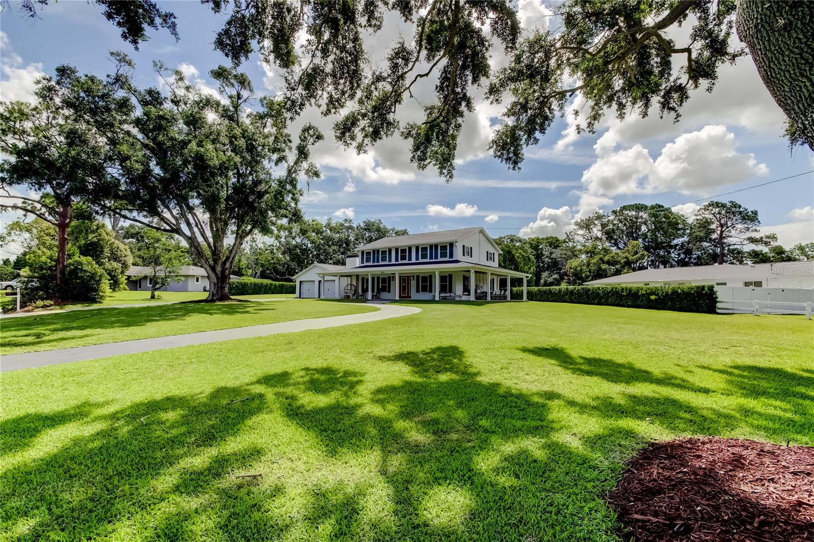 Located in the highly desirable Spanish Trails neighborhood, this beautifully maintained modern farmhouse sits on nearly one acre of private land and offers the perfect blend of charm, functionality, and storm-ready upgrades. With 2,472 heated square feet, this two-story home features 4 bedrooms, 2.5 bathrooms, and a well-designed layout filled with thoughtful touches. The first floor includes a spacious family room, formal living room, elegant dining room, and an eat-in kitchen with hardwood cabinetry, granite countertops, and stainless steel appliances. A former fifth bedroom has been converted into a custom laundry room with a center island, and the entire downstairs showcases hardwood and ceramic tile floors, farmhouse-style doors, and updated finishes. The oversized two-car garage features hurricane-rated doors, epoxy flooring, and new openers. Upstairs, you'll find four spacious bedrooms and two fully renovated bathrooms with quartz countertops and modern tilework, along with original pegged oak hardwood floors and plantation shutters throughout.
Outdoor living is elevated with a 600+ square foot wraparound porch, a screened lanai, grilling area, firepit, and a custom-built shed—perfect as a studio or workspace. The grounds are beautifully landscaped with three freshly trimmed oak trees and a circular driveway. The backyard is an oasis of privacy with a new (2025) steel-reinforced wooden fence along the eastern border of the property, and a row of podocarpus hedges along the southern border of the property. Likewise, the homeowner to the north planted a row of podocarpus hedges, giving the property symmetry, privacy, and protection on all sides.
Major upgrades include a 2023 30-year shingle roof (transferable warranty), Simonton impact windows and PGT doors (lifetime warranty), hurricane-rated garage doors, a newer Lennox dual-zone A/C system (under warranty), and a whole-house Generac generator with a 500-gallon buried propane tank. Additional features include a private-well irrigation system, WiFi-enabled programmable Trim Lights, and front and rear security cameras. This is a rare opportunity to own a fully upgraded, storm-resilient home in one of Dunedin’s most sought-after custom home communities, just minutes from the Gulf, downtown Dunedin, and top-rated schools.