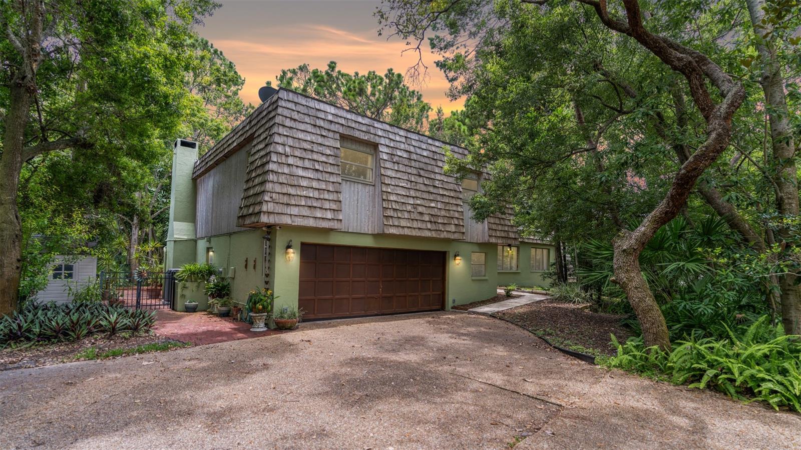 A Rare Architectural Retreat in the Heart of Dunedin
Tucked away on an award-winning, one-acre homesite enveloped in native Florida foliage, this distinctive residence harmonizes thoughtful design with natural beauty—just minutes from the vibrant heart of downtown Dunedin. Conceived, crafted, and owned by a local architect, the home offers over 3,100 square feet of intelligently designed living space, including a 4-bedroom, 3-bath main residence and a separate, air-conditioned studio perfect for artistic pursuits, remote work, or future guest accommodations.
Inside, generous living and dining spaces unfold into a warm and welcoming family room with fireplace, while the expansive island kitchen features custom shaker cabinetry and plentiful workspace—an entertainer’s dream. The primary suite provides a quiet escape with its private balcony perched above the grounds, while oversized secondary bedrooms ensure room to grow, gather, or simply relax.
Recent updates include a 2021 roof, upgraded impact-rated windows and doors, and an oversized two-car garage. Outdoors, the experience is equally compelling: a shaded gazebo, built-in grill, and paver patio are set among lush landscaping certified as a backyard wildlife habitat—blending privacy and purpose with true environmental stewardship.
Located moments from Honeymoon and Caladesi Islands, Clearwater Beach, and Dunedin’s charming shops, cafes, and golf courses, this architecturally significant property offers a rare chance to own a private, nature-forward haven in one of Tampa Bay’s most desirable communities.