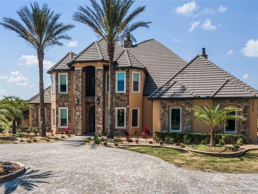 Welcome  to 33645 Grand Champion Lane, Eustis. Imagine a home nestled on over 45 acres of prime Florida real estate with outdoor flourishes one can only dream of. Imagination meets reality with this palatial home in Eustis, complete with a resort-like pool and slide, waterfall, grotto, hot tub and koi pond. The home with over 6,000 square feet under air, has five bedrooms, four baths and two half-baths in the main house, and features two fireplaces, with built-ins and custom millwork throughout. The captivating formal living area offers coffered ceilings with crown moldings and accent lighting, and large picture windows overlooking the pool area. Inside the kitchen, stainless steel appliances with panelized Sub-Zero refrigerator, Miele coffee machine, large gas stove, kettle faucet, prep sink, coffee and wine bar, and walk-in pantry provide all that’s needed for your culinary creations. For your eating pleasure, the dining room offers a tray ceiling, built-in buffet, picture windows with northern exposure while the dinette overlooks the pool and patio area with large picture windows. In the den, you’ll find expansive built-ins with a fireplace accented by stone and slate, an exposed beam ceiling and French doors that open to the pool area. Upstairs, two rooms have access to a balcony at the front of the home and the two upstairs bedrooms have en-suite baths. All bedrooms have hand-scraped Brazilian oak flooring and walk-in closets. Need a workout? A large gym offers floor-to-ceiling mirrors with large windows overlooking the pool area with French doors leading to a large second floor outdoor deck area. Want to be entertained? A billiards and game room keep you occupied, and a 13-seat theater room has a fiber optic starlight ceiling and in-projection screen. Outside, enjoy the cabana with kitchen, Wolf grill, kegerator, outdoor shower and table with fire feature. An outdoor gun range comes with a berm backstop. The detached five-car garage, plus space for an RV, has room for all your vehicles and toys, and an outdoor lean-to can provide additional storage or parking for equipment. A three-bedroom one-bath apartment with 1,440 square feet of space on the second floor above the shop is an open-concept split plan with fireplace and it complements all that this magnificent home has to offer.