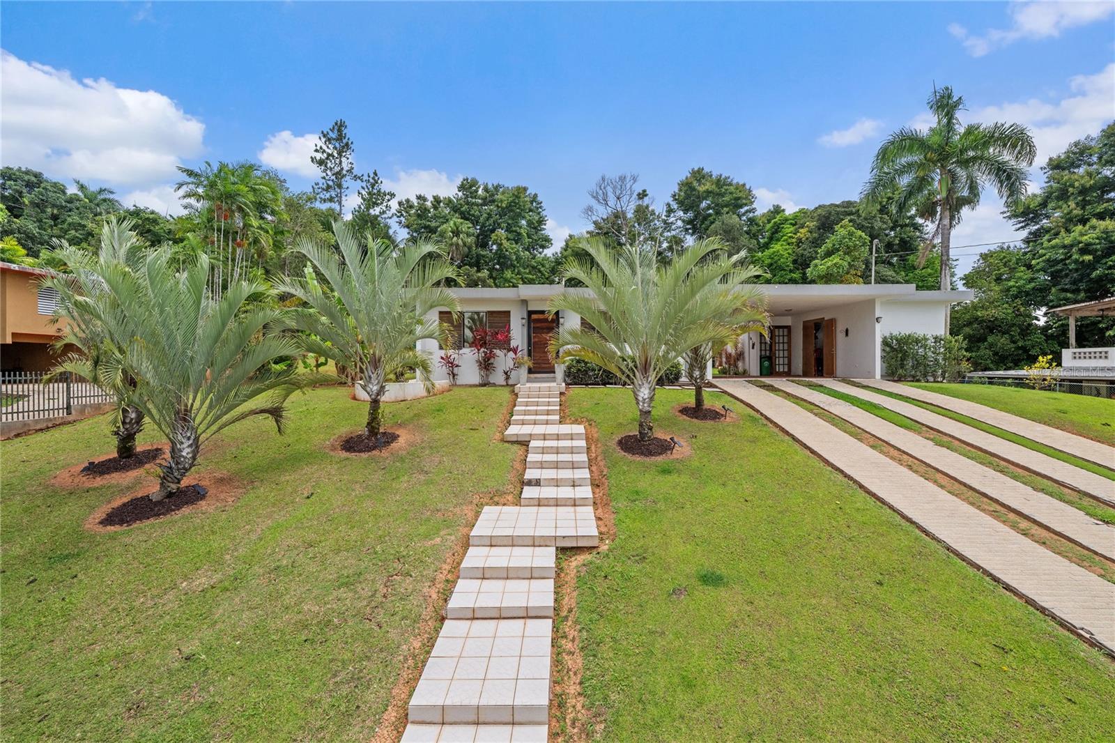 Discover the perfect blend of city convenience and tranquil countryside living in this beautiful one-story home in Lomas del Sol, Guaynabo. This property offers the best of both worlds—easy access to urban life while being surrounded by nature, lush vegetation, and fresh breezes.
Situated on an expansive 2,182 m² lot, this contemporary residence boasts 1,864sq ft. The property features impressive outdoor oasis great for entertaining. The interior showcases an open-concept layout, including a living room, dining area, an inviting family room, and kitchen with top-of-the-line appliances. The house spans three bedrooms with two bathrooms, and a powder room, additionally two flex rooms currently used as an office and storage room, convertible to a private apartment.
Enjoy resort-style amenities including a Salt Water Pool with an Inverter Motor, an outdoor bar with BBQ area, and a fire-pit or lechónera. Designed for comfort and sustainability, the property is fully equipped with a 12k Generator, 23 Solar Panels, 2 Tesla batteries, and a Solar Water Heater. This home invites you to live a lifestyle that seamlessly combines nature, comfort, and convenience. Don’t miss this rare opportunity, call today to schedule your private showing!