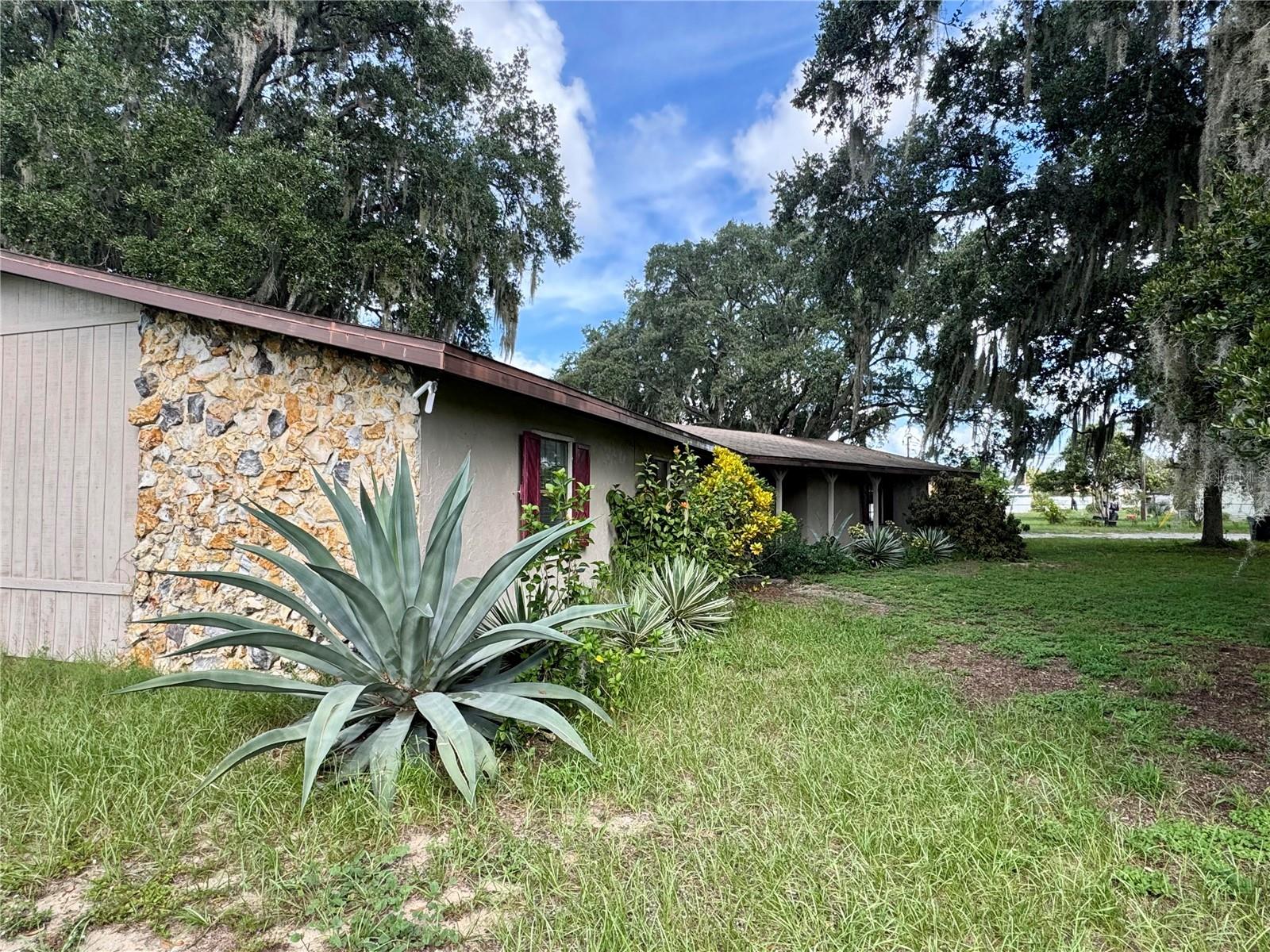 Tucked beneath a canopy of mature oak trees and set on almost two acres, this fully furnished 4-bedroom, 3-bath home delivers space, character, and privacy—with NO HOA. The great room makes an impression with vaulted wood ceilings, exposed beams, a brick accent wall, and a stone fireplace, and it opens to an eat-in kitchen featuring granite countertops, a breakfast bar, stainless steel appliances, and French doors to the backyard for easy indoor–outdoor living. A spacious formal dining room adds flexibility for hosting. The split layout places the primary suite on one side with a bathroom (custom cabinetry, granite, and updated tile shower), while bedrooms two and three share an updated hall bath with dual sinks. The fourth bedroom sits on the opposite side of the home with a nearby third full bath—ideal for guests or a private office. An oversized indoor laundry room with a sink cabinet keeps daily tasks simple. Practical features include a 2-car attached garage with workshop and a large fenced in backyard. The setting is amazing; plenty of room to park a boat or RV, add a large garage/workshop, or explore future options with the county.
The property is located very close to HWY 27 and I-4 for easy access across Central Florida, and approximately 30-45 minutes to Walt Disney World! Schedule your private tour and imagine the possibilities this property offers.
