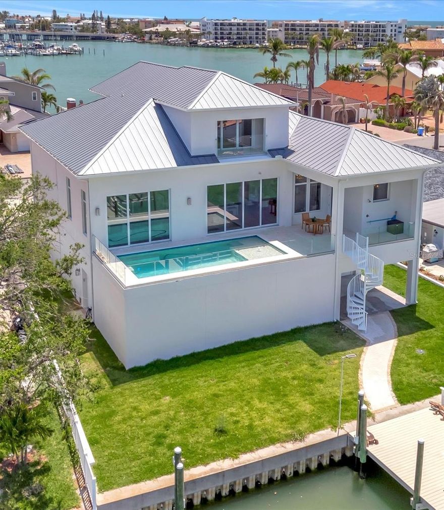 Welcome to your coastal dream retreat, where everyday life feels like a permanent vacation. Nestled on the serene shores of Paradise Island in Treasure Island, Florida, this luxury waterfront home blends striking design with thoughtful, high-end features that make living here as effortless as it is stunning.  From the moment you step inside, you’re greeted by dramatic 14-foot ceilings and 12-foot doors that flood the home with natural light and invite the outdoors in. The expansive living space was designed with gatherings in mind—whether it’s a quiet morning with coffee or a lively evening of entertaining. The chef’s kitchen is both a showpiece and a workhorse, with a striking Quantum Dolce Vita quartz waterfall island, premium Thermador and Bosch appliances, and a Cambria Montgomery quartz wine and coffee bar that turns every pour into an experience.  Take the private elevator from the oversized garage—with space for 10 cars or up to 20 with lifts—and arrive on the second floor, where your private heated pool awaits. Thoughtfully engineered with pilings built specifically to support a second-story pool, it's the perfect place to unwind with sunset views and sea breezes after a day on the water.  This home is built for real peace of mind, with hurricane-ready construction, a 500-gallon buried propane tank, whole-house generator, and dual AC units—because luxury means never having to worry.  The grand primary suite is a true escape, featuring dual walk-in closets, spa-style vanities, a freestanding soaking tub, and a private water closet—all set in luxurious Stoneworld Sono Calacatta Montgomery quartz. Three additional bedrooms offer space for family or guests, while the upstairs loft space flexes effortlessly to meet your needs—home office, fitness studio, game room, or even an extra bedroom.  Whether you're spending weekends boating, lounging poolside with friends, or simply soaking in the view with a glass of wine at sunset, this home delivers the ultimate coastal lifestyle in one of Treasure Island’s most coveted waterfront communities.
Come experience it for yourself—and fall in love with what it feels like to live here.