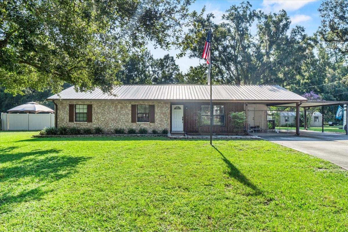 Welcome to Whiskey Oak Ranch, a charming blend of rustic elegance and Florida sunshine. Tucked away on a quiet dead-end road, this 3 bedroom, 2 bathroom ranch-style home rests on 3.74 fully fenced and gated acres, offering space, privacy, and room to roam. The newer metal roof and classic ranch architecture provide timeless appeal, while mature oaks sway in the breeze and frame the rural backdrop. Step inside to find gleaming hardwood floors that flow through most of the home, a spacious primary suite with ensuite bath, and a bright indoor laundry room for everyday convenience. The kitchen and living spaces open seamlessly to a large, screened lanai that’s an entertainer’s dream, complete with a hanging hammock swing set, cast iron fireplace, bar seating with stools, mounted fans, and a statement pool bar light. Outdoors, enjoy front and rear irrigation systems, an in-ground pool, multiple outbuildings, and both attached and detached carports for vehicles, toys, or equipment. Whether you’re hosting friends’ poolside, tending to your gardens, or relaxing under the shade of your oaks, Whiskey Oak Ranch delivers the laid-back country lifestyle you’ve been searching for.