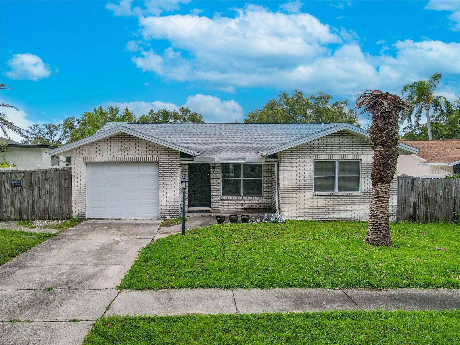 Well-maintained 2-bedroom, 2-bath home featuring a clean, low-maintenance exterior with light brick facade, a welcoming covered entry, and a fenced side and backyard for privacy. A single-car garage with a wide driveway provides ample parking. Major updates include a 2019 roof, 2019 A/C, and double-pane windows for energy efficiency.
Step inside to a bright, open-concept living and dining area with neutral tile flooring featuring decorative inlays and a mirrored accent wall that enhances natural light and the sense of space. The living room’s large front-facing windows and ceiling fan create a comfortable, inviting atmosphere, while the dining area flows seamlessly into the kitchen and offers sliding glass doors to a sunny Florida room.
The kitchen is designed for both function and style, featuring abundant wood cabinetry, granite-look countertops, a tile backsplash, and a window over the sink for added light. Appliances include a range, microwave, and dishwasher. A convenient access door to the garage makes unloading groceries a breeze.
The spacious primary bedroom offers tile flooring, dual ceiling fans, and multiple windows for natural light. Sliding glass doors lead directly to the Florida room, and the updated en-suite bathroom features a granite-topped vanity, modern fixtures, and a walk-in shower with mosaic tile accents, sliding glass doors, and grab bars for safety. Dual entry points from both the bedroom and hallway add convenience.
The second bedroom features tile flooring, a ceiling fan, large windows on two walls, and a wall-to-wall double closet. The second full bathroom includes a tub/shower combo with sliding glass doors, grab bars, and a mirrored vanity with storage.
The attached garage offers built-in shelving, a laundry area with washer, dryer, utility sink, and extra storage. Outdoors, the expansive fenced backyard boasts a concrete patio perfect for dining and entertaining, a level grassy area for pets or play, and plenty of room to add a pool or garden.
Located close to shopping, dining, medical facilities, and beautiful Gulf beaches, this home offers comfort, convenience.