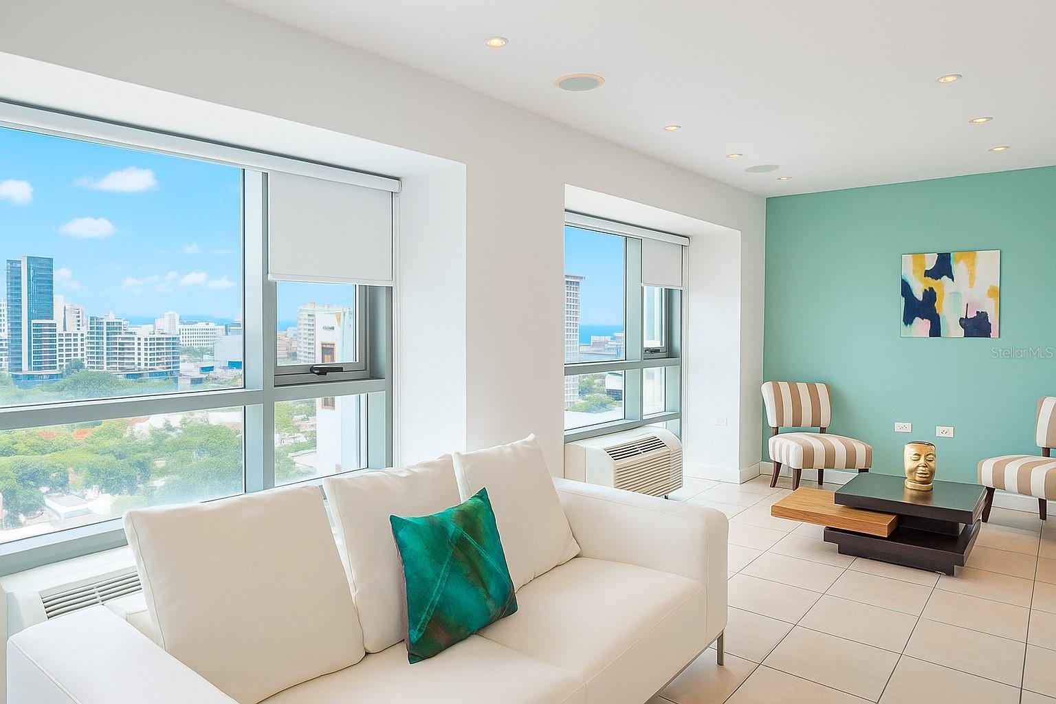 Modern and bright apartment located in the prestigious Gallery Plaza in Condado, San Juan. This spacious unit showcases stunning panoramic city views through floor-to-ceiling windows that fill the interior with natural light. Featuring an open-concept layout, the living and dining areas seamlessly connect with a contemporary kitchen equipped with two-tone cabinetry, quartz countertops, and stainless steel appliances.
The primary bedroom offers a peaceful retreat with clean lines and high-quality finishes. Residents enjoy exclusive amenities, including a resort-style swimming pool, a fully-equipped fitness center, 24/7 security, and concierge service. Additional highlights: full backup generator, water cistern, and convenient access to restaurants, shops, entertainment, and the beach.
Ideal for those seeking sophisticated urban living in one of San Juan’s most vibrant neighborhoods.