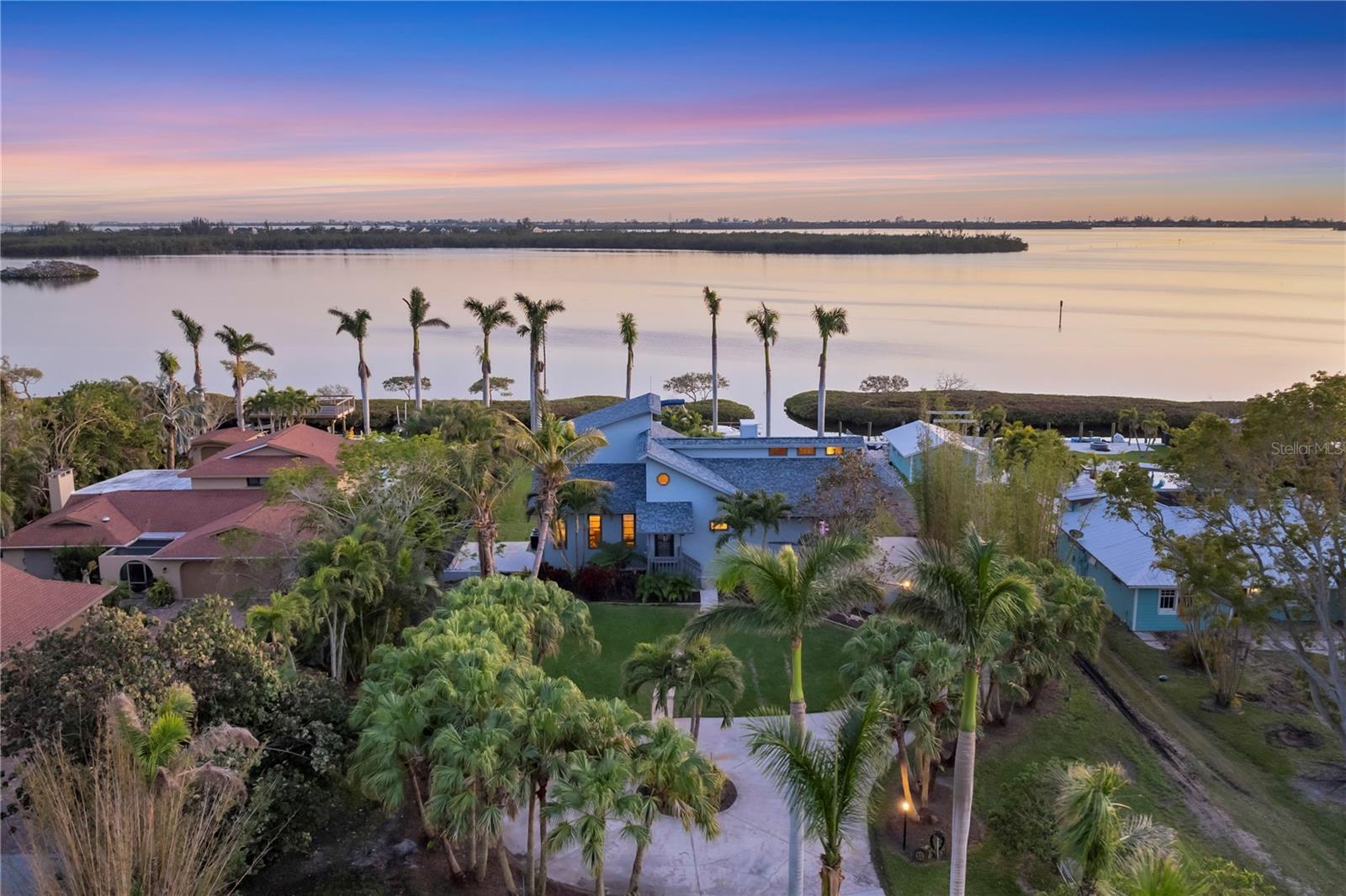This exceptional 1-acre bayfront estate offers “Old Florida” charm with panoramic water views of Paradise Bay with direct boating access to Sarasota Bay and no fixed bridges to the Gulf. The winding drive, lined with majestic royal palms, welcomes you to a tropical haven, complete with beautifully landscaped grounds kept lush with a well irrigation system. Relish the natural beauty of palms, fruit trees, bamboo, a magnificent magnolia, and vibrant tree fern that surround this tranquil retreat. The coastal contemporary designed home boasts three spacious living levels, each with outdoor decks to take in breathtaking views. The ground level features an oversized garage, additional covered parking, storage space, and a concrete parking pad perfect for RV or boat storage. A grandfathered one bedroom, one bath in-law apartment with kitchenette offers privacy and comfort, along with a stair lift to access the second level. The second level offers a large living and dining area, a fully equipped kitchen, office/den, guest bedroom and guest bath with antique claw foot tub, bonus room/possible bedroom with built-in cabinets and sink. The kitchen has brass ceiling tiles, plentiful cabinet storage, granite countertops and a breakfast bar island with water views. A built-in saltwater aquarium framed in keystone adds a unique touch to the living room, while the adjoining dining room showcases a beautiful keystone-covered gas fireplace. Gorgeous tongue-and-groove hardwood flooring, combining cherry, red oak, white oak, maple, and walnut, creates warmth and elegance throughout. Vaulted ceilings with clerestory windows fill the space with natural light and highlight the home’s dramatic design. A spiral staircase with solid brass railing leads to the third level, where you'll find the spacious primary suite—complete with its own private balcony offering spectacular waterfront views. The ensuite bath features dual sinks, a separate shower, and a WC. The property boasts 100 feet of pristine waterfront, with a concrete seawall, boat davits, power/water, and a fish cleaning station. The natural mangrove barrier provides protection for the canal, and the location provides easy access for boating, fishing and watching dolphins, manatees, and a variety of birds, including the nearby osprey nest, from the comfort of your own backyard. Located just minutes from the beautiful beaches of Anna Maria Island and the charming Cortez Fishing Village, this estate is convenient to top-tier seafood restaurants and waterfront dining options. This is a rare opportunity to own a prime piece of Sarasota Bay waterfront—don’t miss your chance to make this exceptional property your own!