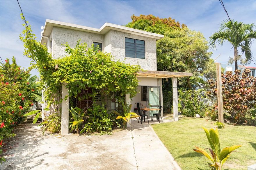 From this tucked-away vantage point, the bay of Isabel Segunda unfolds right before your eyes. Perched like a mirador, the home offers a front-row seat to the charming comings and goings of the ferry and local fishermen, all set against the stunning backdrop of the main island. As the sun sets, the north-facing terrace becomes a spectacular viewing point, blending the vibrant life of the port with peaceful, golden-hour views—just a one-minute walk from the water.

Tucked away at the end of a cul-de-sac with a private entrance and lush gardens, this property offers a rare combination of seclusion and convenience. The grounds are beautifully landscaped with swaying palms, ornamental foliage, and a variety of fruit-bearing plants that add color, fragrance, and flavor to the outdoor experience. A green walkway patio surrounds the home, leading to open-air nooks, outdoor showers, and built-in benches that invite relaxation and privacy.

The home features an eclectic mix of design materials—polished cement, warm wood accents, and colorful decorative tiles—creating a vibrant, textured aesthetic that feels both tropical and timeless. The property consists of two separate apartments, offering flexibility for guests or multi-family living.

The lower apartment features two bedrooms with ensuite bathrooms connected by a spacious common area. It includes a large kitchen, indoor and outdoor dining spaces, and a cozy lounge that opens directly to the courtyard. This distinctive unit evokes the charm of old San Juan with its inviting, lived-in character.

Upstairs, the second apartment feels like a boutique loft. High ceilings, expansive sliding doors, and windows create a breezy, light-filled space that opens onto a massive terrace—perfect for lounging or enjoying the deluxe outdoor shower while taking in panoramic views of the bay. This unit also includes a dedicated workspace, a comfortable living area, and an ensuite bathroom.

While the entire home is air-conditioned, the natural breezes at this charming town villa are unforgettable. There’s also ample space to add a covered garage and plunge pool, making this already enchanting property even more ideal.