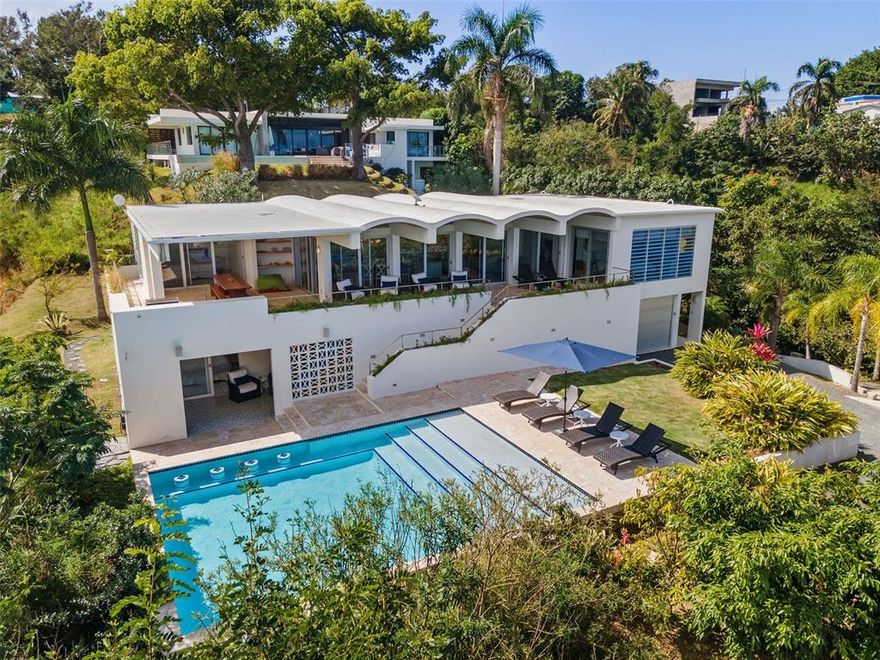 Contemporary Marvel with Sweeping Ocean Views – Designed by renowned New York architects Big Prototype, this magnificent single-family estate resides in Barrio Puntas - the most sought-after community in Rincon, known for spectacular ocean vistas and laidback elegance. This massive 6,300 square foot 5 bedroom, 4.5 bathroom home was designed to fully maximize it's premier hilltop location showcasing ocean views from nearly every room. From sunrise to sunset, the lush greenery, azure ocean, and fiery pinks of Rincon’s famed sunsets are your personal panoramic entertainment. Spread out over two floors, the barrel-vaulted ceiling brings a sense of amplitude and maximizes the open-plan living concept with an immense 30 ft x 40 ft great room. A surround sound system and a custom-built projection screen are hidden to allow for a movie theater quality experience, without sacrificing views or wall space. A separate TV area and offshoot of the living room provides even more space for lounging. Enjoy ocean views from the fully renovated kitchen featuring brand new LG appliances, an oversized island perfect to use as a breakfast bar and luxurious white quartz countertops throughout. The expansive terrace features a renovated outdoor kitchen and a large custom dining table providing multiple sizable spaces for entertaining Al Fresco. The main level has 3 bedrooms and 2 bathrooms off the principal living area, each with a sense of privacy and openness off the main terrace to appreciate the scenic views. On the second lower level, 2 bedrooms and 2 full bathrooms provide even more space and privacy. From the first level primary suite, an ensuite bathroom and private outdoor terrace provides the outmost peaceful retreat. Step out onto the charming colorful tile, inspired by 1960s spanish revival, and curl up with a book or dive directly into the oversized, heated saltwater infinity pool with swim-up bar. Celebrating its indoor-outdoor living concept, this palatial abode was meticulously designed as an entertainer’s dream. An outdoor shower and bathroom are thoughtfully placed off of the pool area. Large storage areas and a garage afford residents the ability to store every bit of gear needed to fully enjoy lounging at the beach and watersports. Relish the laid-back luxe ambiance that embodies the Rincon lifestyle - swimming, surfing, boating, hiking, fine dining, tranquility, nightlife, and the best sunsets in the Caribbean. 

The home includes an eco-friendly greywater collection system that optimizes water collection as well as a full cistern and generator offering its residents all the modern comforts expected in a home of this stature.  
 
Live or invest in the most exclusive sector of Rincon, located on the West Coast of Puerto Rico and known to be the surf capital of the Caribbean. A convenient 30 minute drive to the Aguadilla Rafael Hernandez Marin Airport, with direct daily flights from New York City, and other important city hubs make it an ideal destination in Puerto Rico. 

Get informed about Puerto Rico's Act 60 Tax Incentive Program. Let us help you call this beautiful island HOME. Learn More: https://www.taxincentivespuertoricoinfo.com/