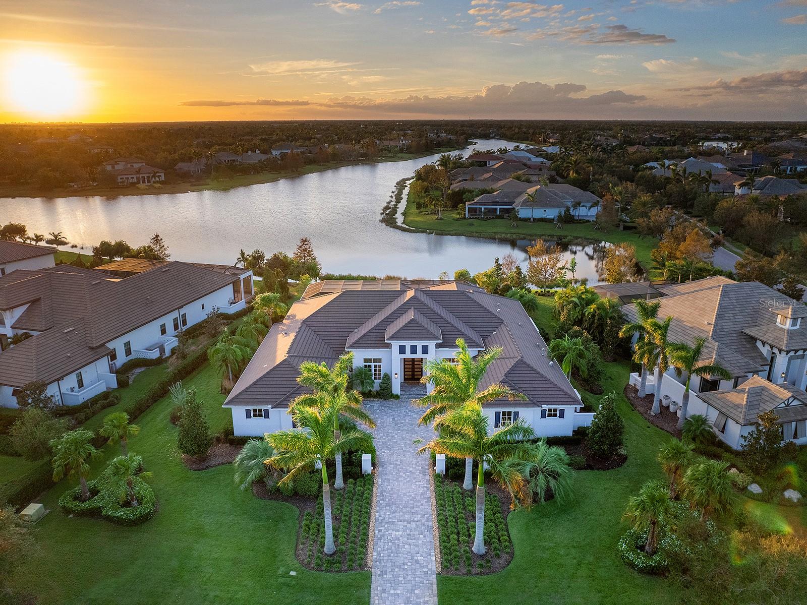 Welcome to Sophisticated Living in The Lake Club of Lakewood Ranch! This 2018 custom Anchor Builders residence exhibits quality construction, intentional design and high-end finishes. Enjoy a spacious .6-acre lot, over 110 feet of lakefront views and a long paver driveway flanked by towering palms, courtyard entry, and upgraded landscaping. You are welcomed by custom double impact glass and iron front doors to the open floor plan graced by oak wood flooring, neutral color palette, and expansive views of the lake beyond. The spacious great room offers a cozy place to gather by the linear fireplace, plus custom beam ceiling, built-in shelving, and pocketing impact sliding glass doors to the lanai. The executive kitchen showcases the perfect blend between modern white cabinetry and quartz counters with full-height backsplash, and warm touches with espresso-stained cabinetry. Guests will gather around the central island to watch the chef perform culinary magic at the Thermador induction cooktop, and then enjoy meals at the casual dinette with custom dry bar, or the formal dining room with designer chandelier. Additional smart upgrades in the kitchen include custom cabinetry with spice drawers and dish storage, Wolf built-in microwave and wall oven, Sub-Zero refrigerator with freezer drawers, and reverse osmosis system. Even catering is made easier with an oversized walk-in butler-style pantry including a full-size wine refrigerator. Your primary suite wing offers a stately study, and convenient multi-purpose room that’s currently used as a fitness room but could also be an art studio, hobby-space, or additional office. The primary bedroom showcases the stunning lake views through large clear windows, and has a seating area, geometric tray ceiling, and custom dual walk-in closets designed with shelving, storage, hanging rods, built-in hampers, and more. Make every day a spa day in the primary bath with walk-in shower featuring multiple showerheads and a frameless glass enclosure, modern soaking tub, built-in towel warmer, dual sinks on large vanity, and custom textured tile feature wall. Guests can relax in their own separate en-suite bedrooms with ample room for king-size beds, walk in closets, Plantation shutters, and walk-in showers. The rear of the home boasts of a bonus room with dry bar, sliding glass doors to the lanai, adjacent powder bath, and a built-in closet to easily turn into a 4th bedroom. The travertine lanai will quickly become your favorite space with covered entertaining and dining areas, custom outdoor kitchen with grill, fenced dog run, and sparkling heated saltwater pool with large sunbathing shelf and sunken spa, all surrounded with custom colonnade screen enclosure with Clearview panels to enjoy the view. This home offers an amazing amount of storage with a “Florida basement” air-conditioned storage room, built-in mudroom shelving and large laundry with cabinetry and linen closet conveniently located near the primary suite. With 4 total attached garage spaces (2 being air conditioned), you will have plenty of space for cars, golf carts, kayaks and still storage space to spare! Peace of mind is secured with 2019 whole-house generator, impact windows and sliders, water softener and filtration, surge protector and more. The Lake Club is a premier, gated community including a Grande Clubhouse, restaurant, pool, tennis, pickleball, playground, basketball, Linear Park, fitness center, dog park and interlinking lakes.