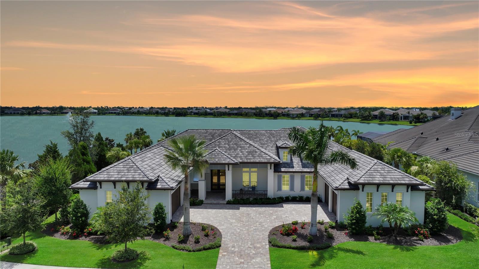 An exceptional expression of Florida luxury, this custom-built, Island-inspired estate by Anchor Builders enjoys an extraordinary setting with wide-open lake views, unmatched privacy, and no neighboring homes in front or to one side—offering a rare sense of space in the exclusive Lakeview Estates section of The Lake Club. Built in 2021 with hurricane impact glass and a whole-house generator for peace of mind, this refined expansion of the Marquesas floor plan offers nearly 5,400 square feet of thoughtfully designed living space with four spacious bedrooms, a private office with custom built-ins, an impressive bonus room, and split garages for four vehicles plus a golf cart. Rich hickory wood floors, intricate ceiling and wall details, and two gas fireplaces enhance the timeless interior, while zero-corner sliders create seamless flow to an extraordinary outdoor living area. The 50-foot saltwater pool and spa, surrounded by Shellock pavers, is paired with a full outdoor kitchen equipped with FireMagic grill, side burners, fridge, sink and bar offering a seamless extension of the home’s luxurious living spaces. Inside, the professional grade kitchen is appointed with finely-crafted hardwood cabinetry, Sub-Zero and Wolf appliances, a generous walk-in pantry, and a wine bar complemented by a Sub-Zero wine fridge. Behind the scenes, high-end smart home technology manages lighting, motorized shades, security cameras, pool functions, and audio, while enterprise-grade Ubiquiti networking ensures flawless connectivity. Additional features include a two private water closets in primary en suite, mosquito misting system, three EV chargers, and a 14x14 air-conditioned interior Florida basement with refrigerator—perfect for secure storage or overflow pantry use. This is an extraordinary opportunity to enjoy a luxurious lifestyle in Lakewood Ranch’s most prestigious gated enclave. Residents of The Lake Club enjoy world-class amenities, including a guard-gated entrance, a vibrant clubhouse, a restaurant and bar, two resort pools, fitness facilities, sports courts, fishing, and scenic trails. Located in Lakewood Ranch, the nation's top-selling multi-generational community, this exceptional residence is just minutes from premier shopping, dining, top-rated schools, and the Gulf Coast's pristine beaches.