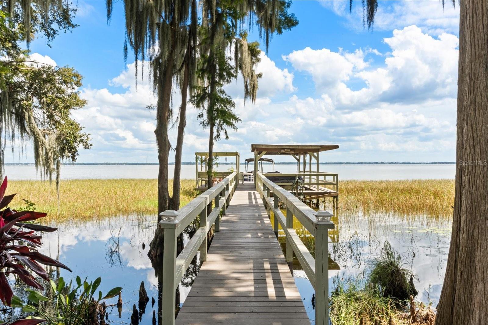Welcome to your personal paradise on Lake Eustis, offering a premium lakefront lifestyle with unparalleled boating access to the famous Harris Chain of Lakes. This unique property spans nearly 1.5 fenced acres with 95 feet of pristine shoreline, a private dock, boathouse, and boat lift, your gateway to endless days of fishing, water sports, and leisurely cruises to waterfront restaurants.
The main residence is a charming 3-bedroom, 3-bath home designed to capture breathtaking lake views from every angle. Inside, vaulted ceilings and a wall of picture windows create a bright and airy atmosphere. The updated kitchen is a chef's delight. The primary suite is a private retreat with stunning lake views, walk-in closets, and a spa-like bath. Upstairs, you’ll find two additional bedrooms also offering beautiful lake views, along with a full bath. An oversized garage includes a convenient full bathroom.
Adding to the property's appeal is a separate, fully equipped in-law suite, complete with a living room, kitchen, bedroom, walk-in closet, and private bath. This versatile space is perfect for guests, family or can serve as a lucrative short-term rental, ideal for visiting fishermen during bass tournaments or travelers seeking a serene escape.
Outdoor living is a dream with an 18-foot swim spa, mature fruit trees (avocado, blood orange, and fig and more), and a spacious 12x24 Lark storage shed. The new roof (8/2025) and newer A/C units provide peace of mind, allowing you to focus on making memories. This is more than just a home, it's the complete lakefront package, blending an idyllic lifestyle with income-generating potential.
