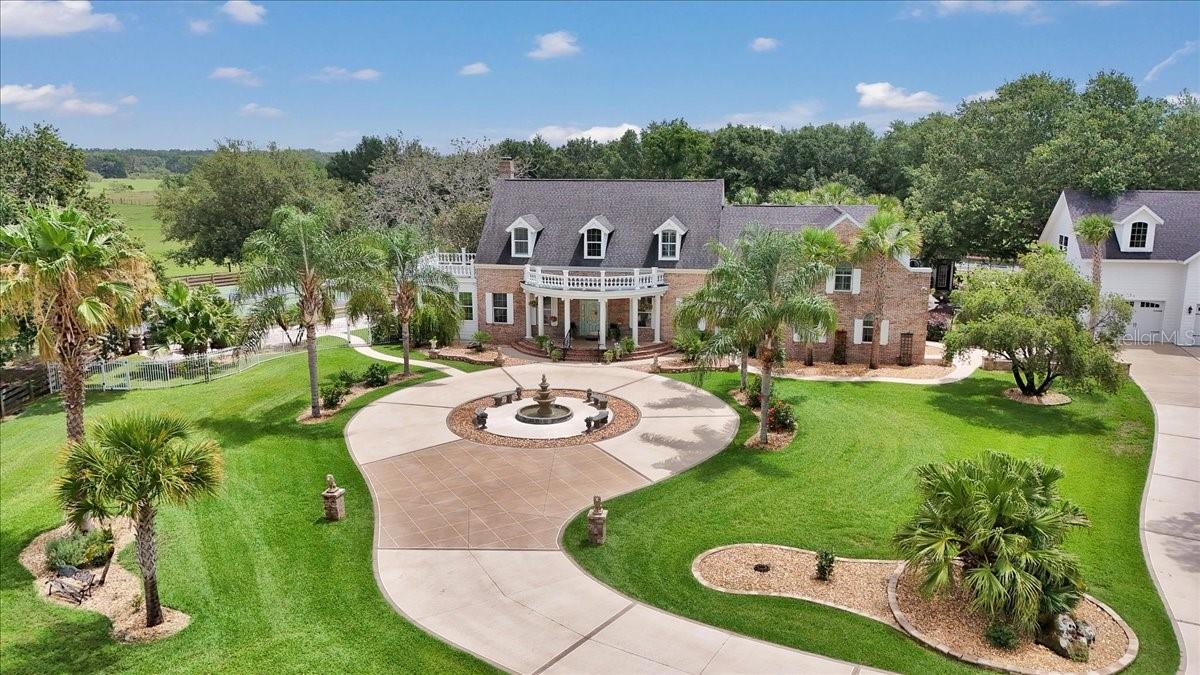 Welcome to paradise in Oxford! This is a rare opportunity to own a one-of-a-kind luxury compound—private, peaceful and ideally within two miles of The Villages. Just five miles from Lake Sumter Landing Market Square, you’ll enjoy easy access to shopping, dining, nightlife, movies and live music. On a beautifully landscaped 6-acre corner lot with two gated entrances, this meticulously designed estate offers nearly 9,000 square feet of total living space across multiple structures. The property is the ultimate entertainer’s dream and a private oasis like no other. The main residence features five bedrooms, three full baths and two half baths. The primary suite is on the main floor, along with a formal living room, formal dining room, a cozy family room with gas fireplace, a workout room and all-season sunroom with dual south-facing french doors. The heart of the home is the eat-in kitchen with a Cambria quartz island, ideal for gatherings and everyday living. Upstairs, a bonus family room connects to four bedrooms, one with a private en suite and two sharing a Jack-and-Jill bath. Go outside to your private resort-style retreat featuring an expansive covered lanai, two cabanas, two pickleball courts, an outdoor kitchen, game room, tavern, guest cabin, she shed, man cave, bocce ball and shuffleboard courts. The centerpiece is a concrete/gunite saltwater pool with tile accents, six waterfalls and deck jets—surrounded by lush landscaping, fountains, a peaceful pond, and an oversized pool house with a changing room and fireplace. Car enthusiasts will love the oversized four-car garage with epoxy floors, and upstairs, enjoy a full movie theater and spacious craft room for creative pursuits or additional living quarters. A second detached four-car garage offers even more space for vehicles, ATVs, boats or toys. Several outdoor structures offer flexibility for ADU conversion, making this estate ideal for multi-generational living, potential rental income or luxury guest accommodations. There’s even a beautiful pasture out front so bring a few animals and enjoy the tranquility of country living. Schedule your private showing today and experience this one-of-a-kind compound for yourself.